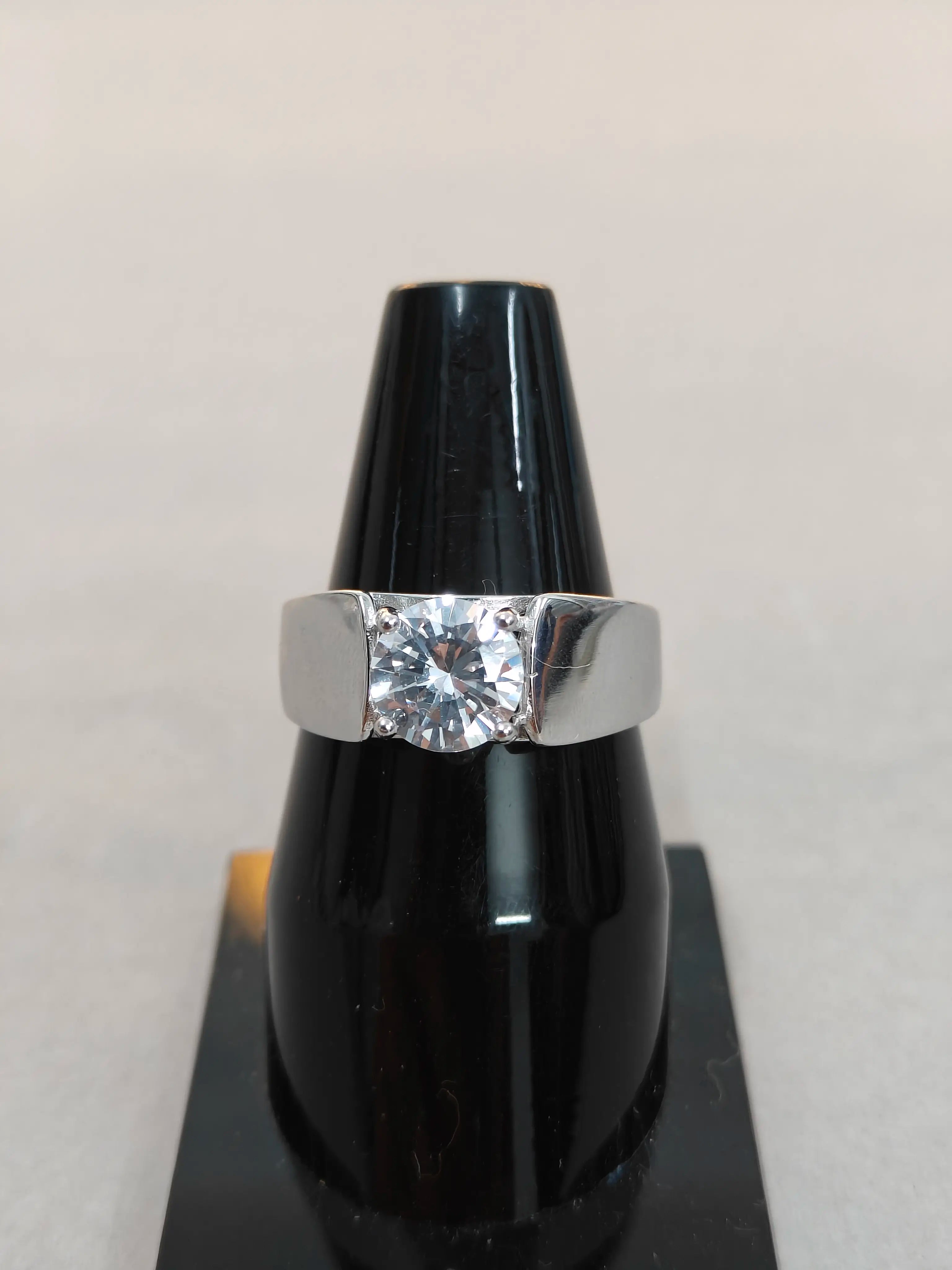 Silver ring with a diamond on a black stand against a light gray background