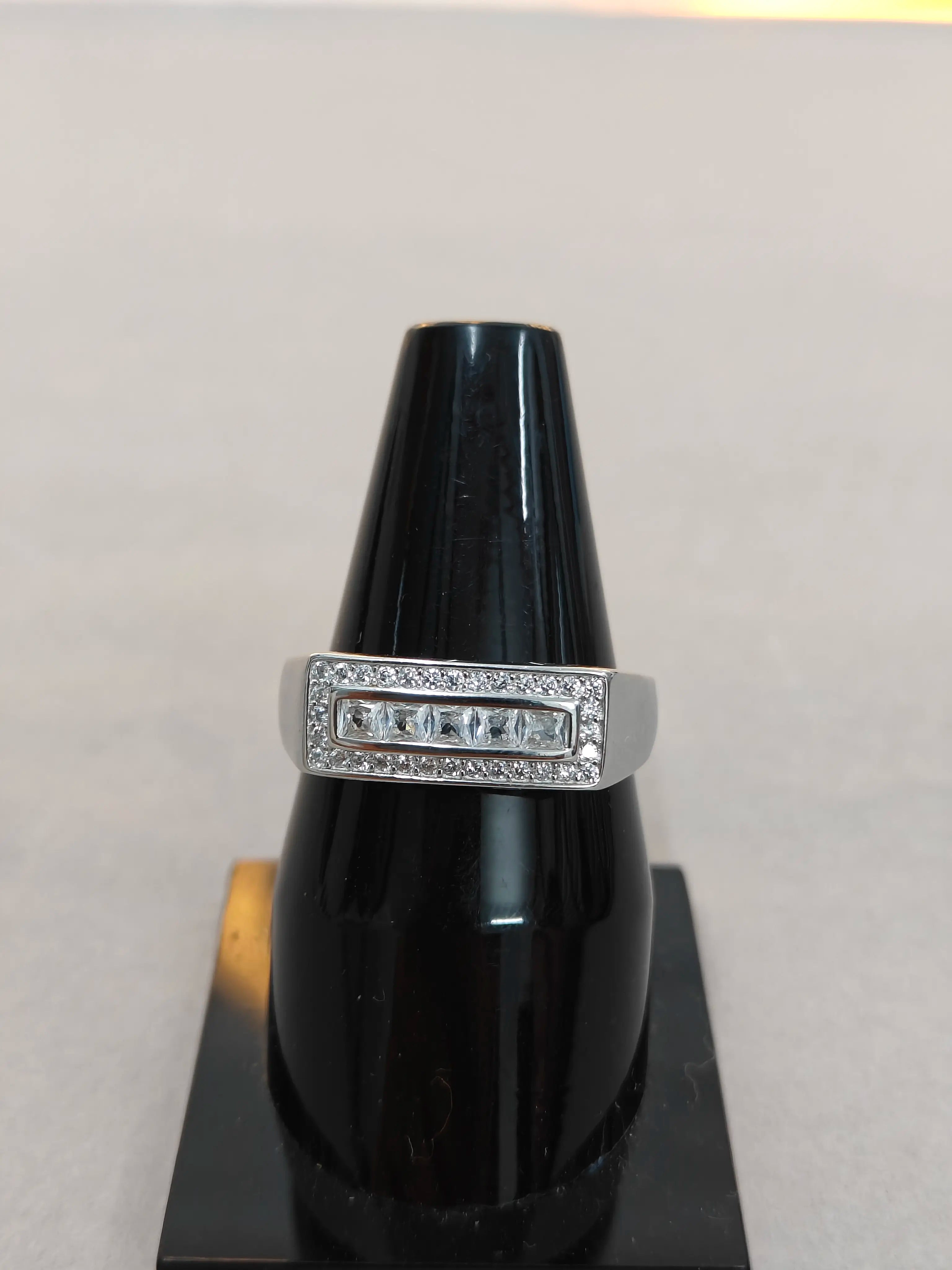 Silver ring with gemstones on a black stand against a light gray background