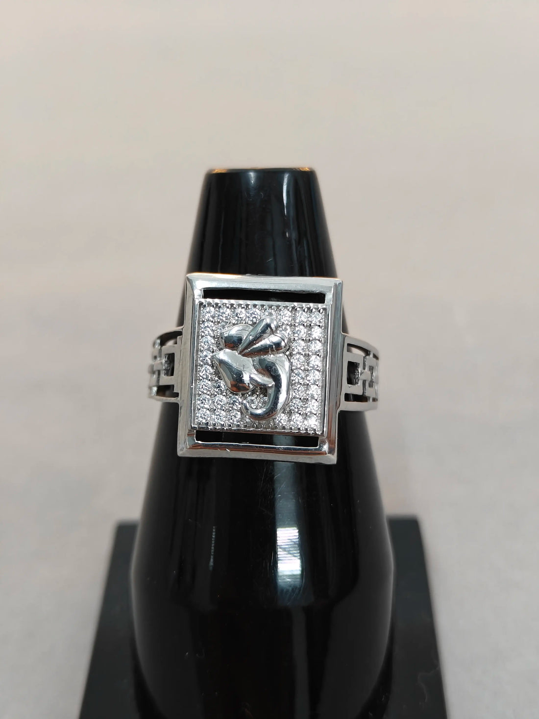 Silver ring with gemstones on a black stand against a light gray background