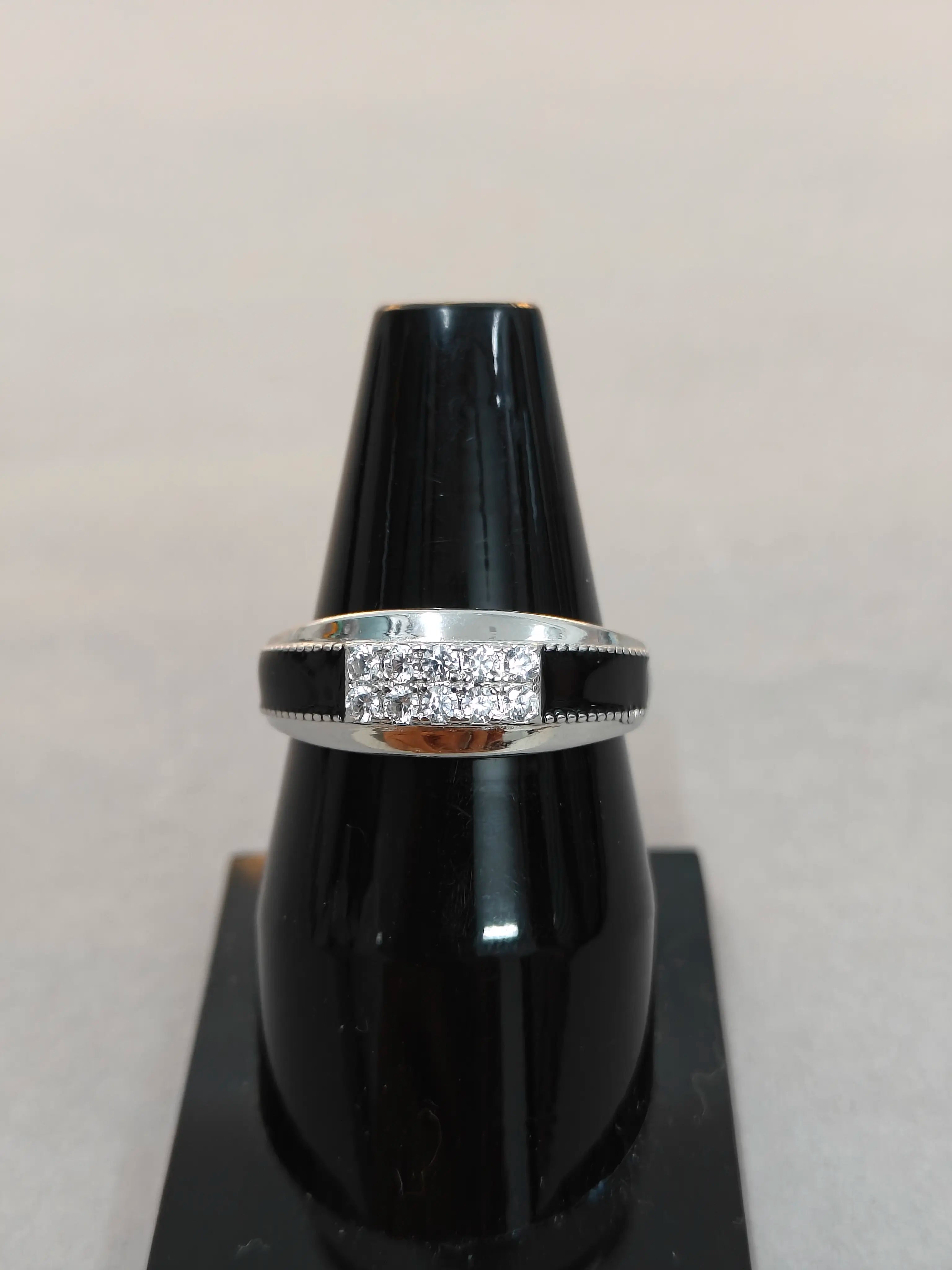 Silver ring with embedded stones on a black stand against a light gray background