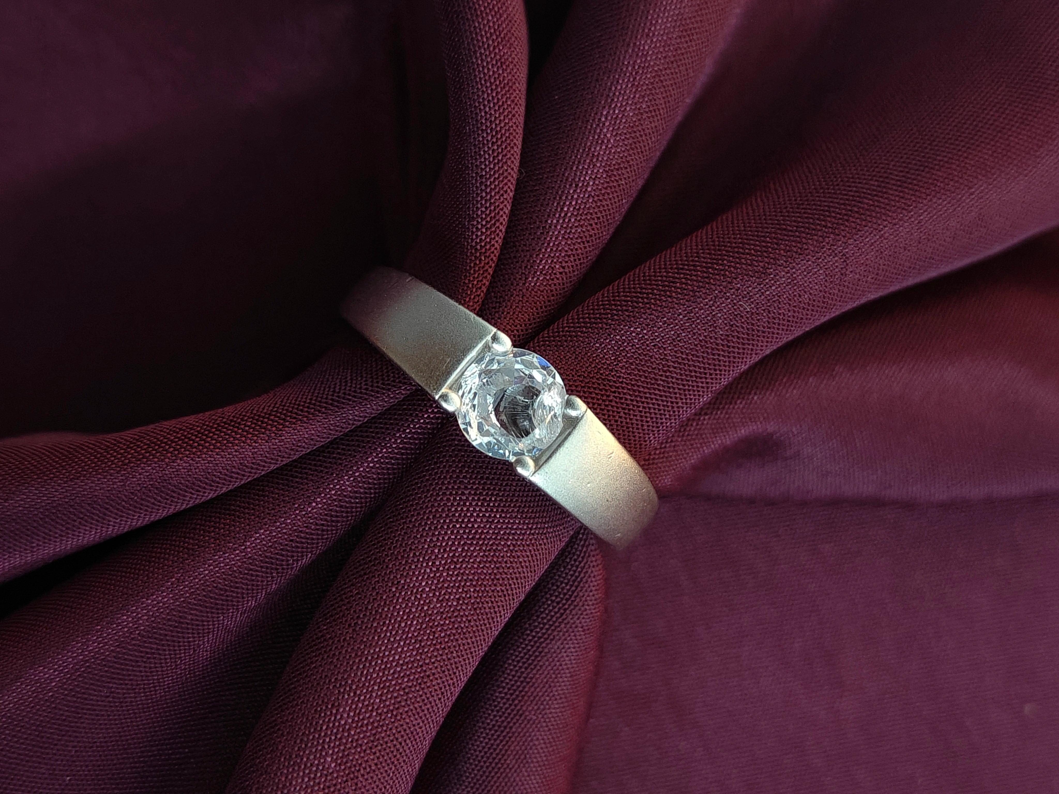 Silver ring with a diamond on a maroon fabric background
