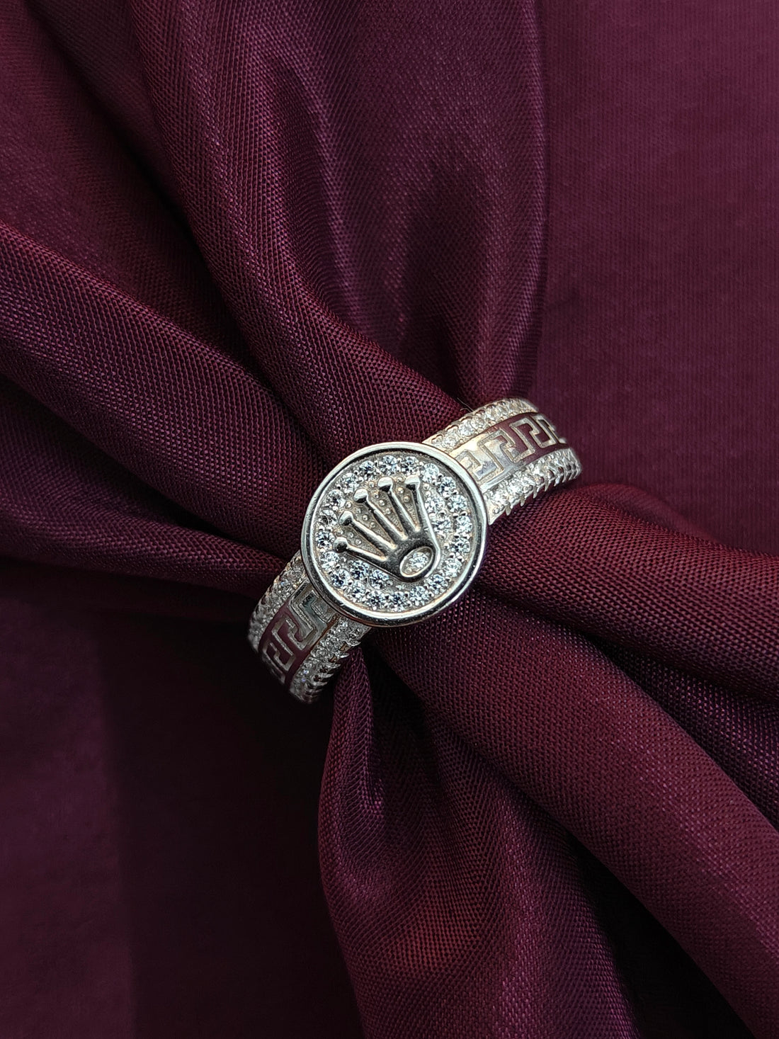 Silver ring with a logo on a maroon fabric background
