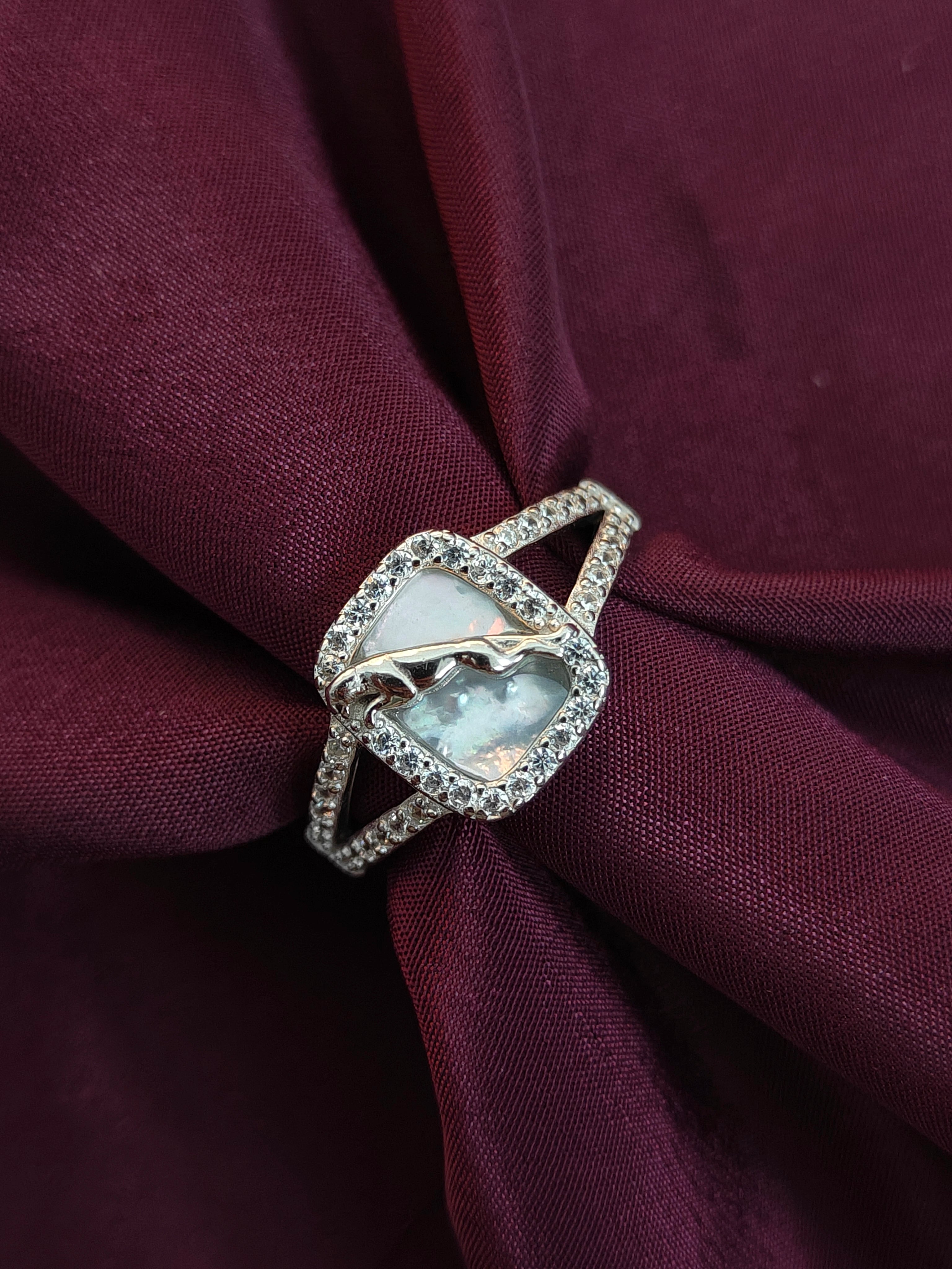 Silver ring with a large central gemstone and smaller stones on a burgundy fabric background