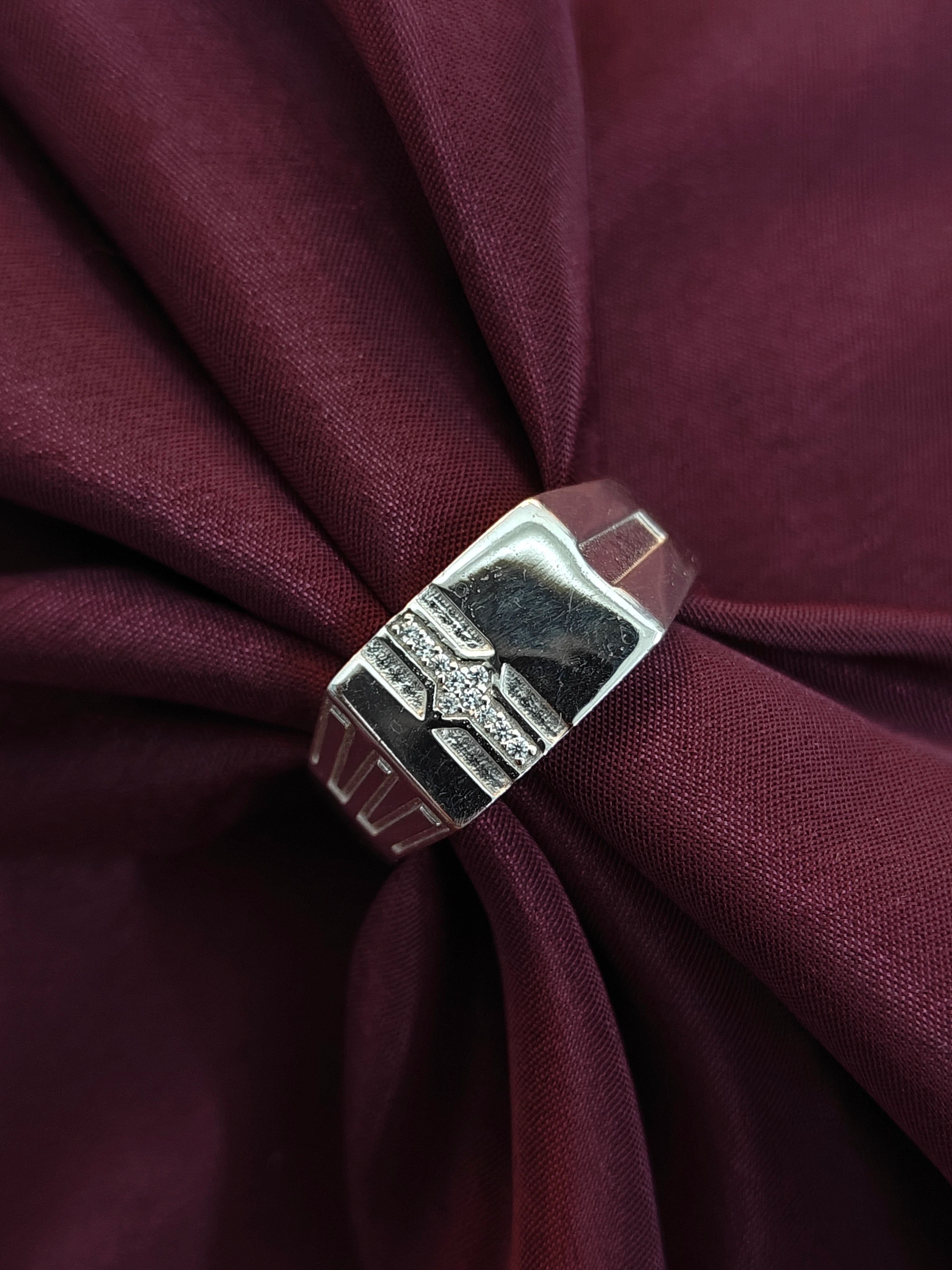 Silver ring with geometric design on a burgundy fabric background