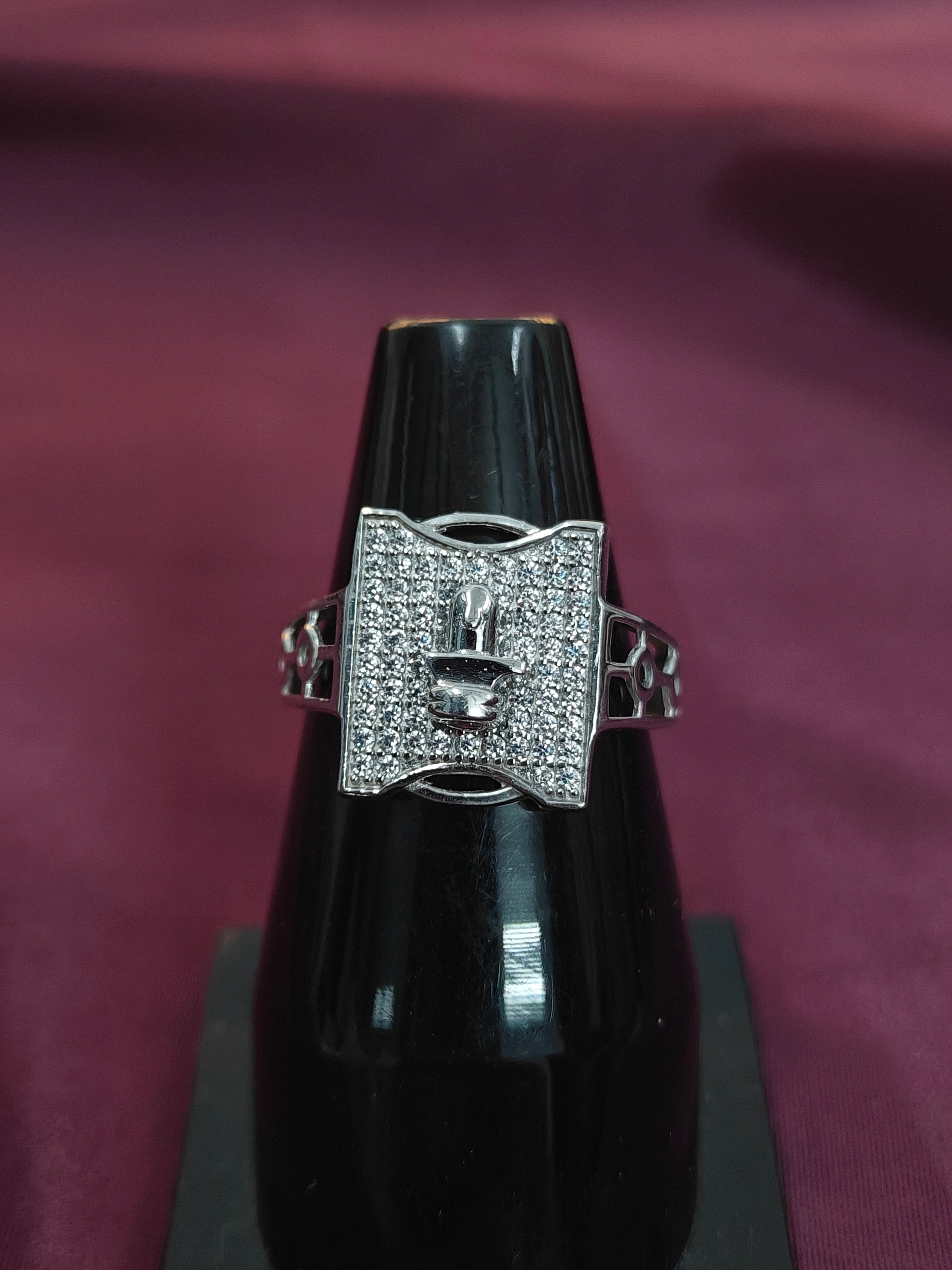 Silver ring with a large central gemstone on a black stand against a maroon background