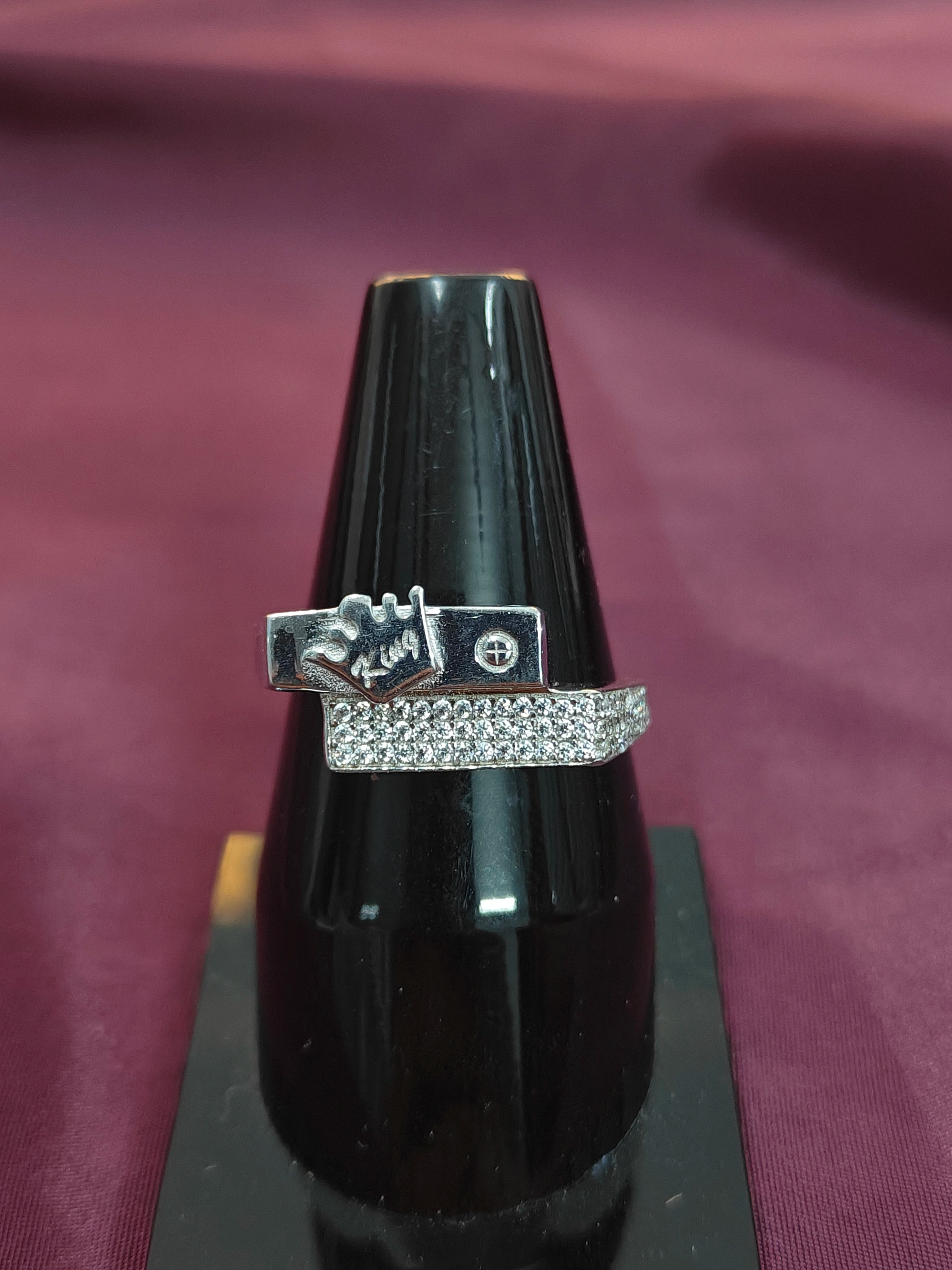 Silver ring with a decorative design on a black stand against a purple fabric background