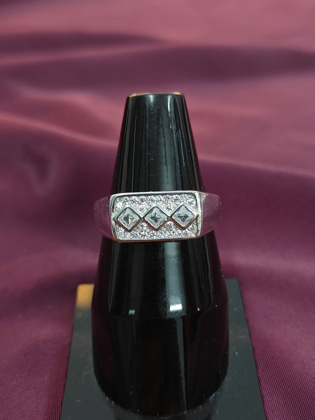 Ring with diamond-like stones on a black stand against a purple fabric background