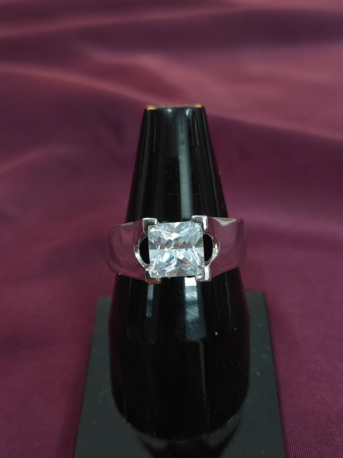 Silver ring with a large diamond on a black stand against a purple fabric background