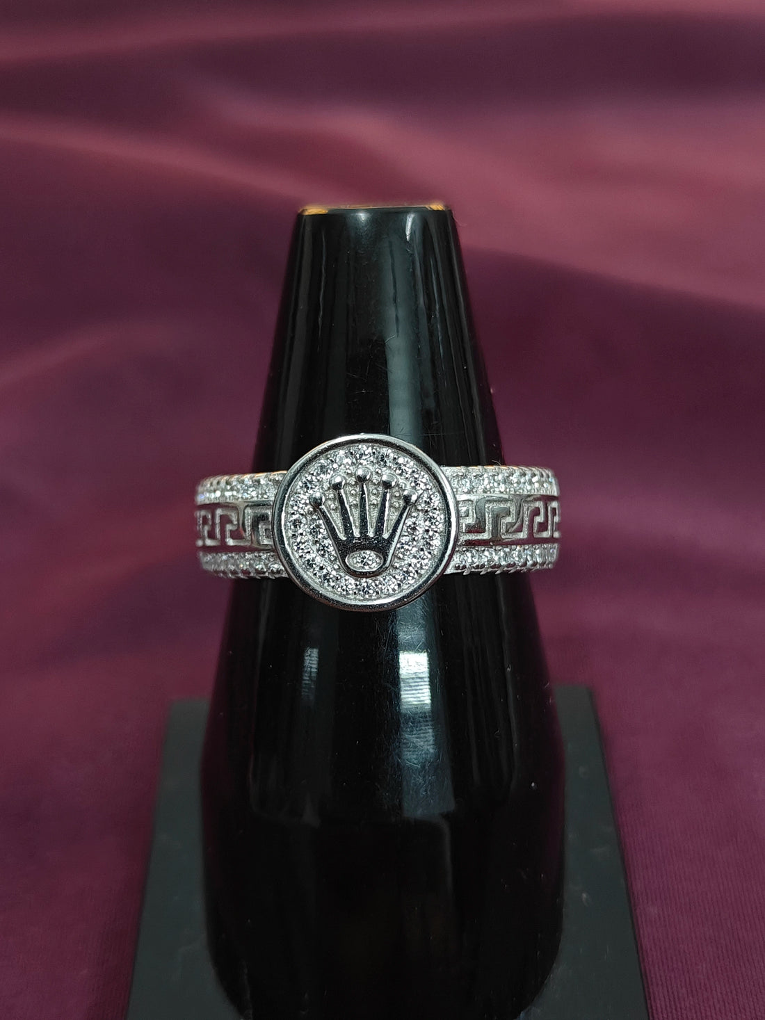 Silver ring with a prominent design on a black stand against a purple fabric background