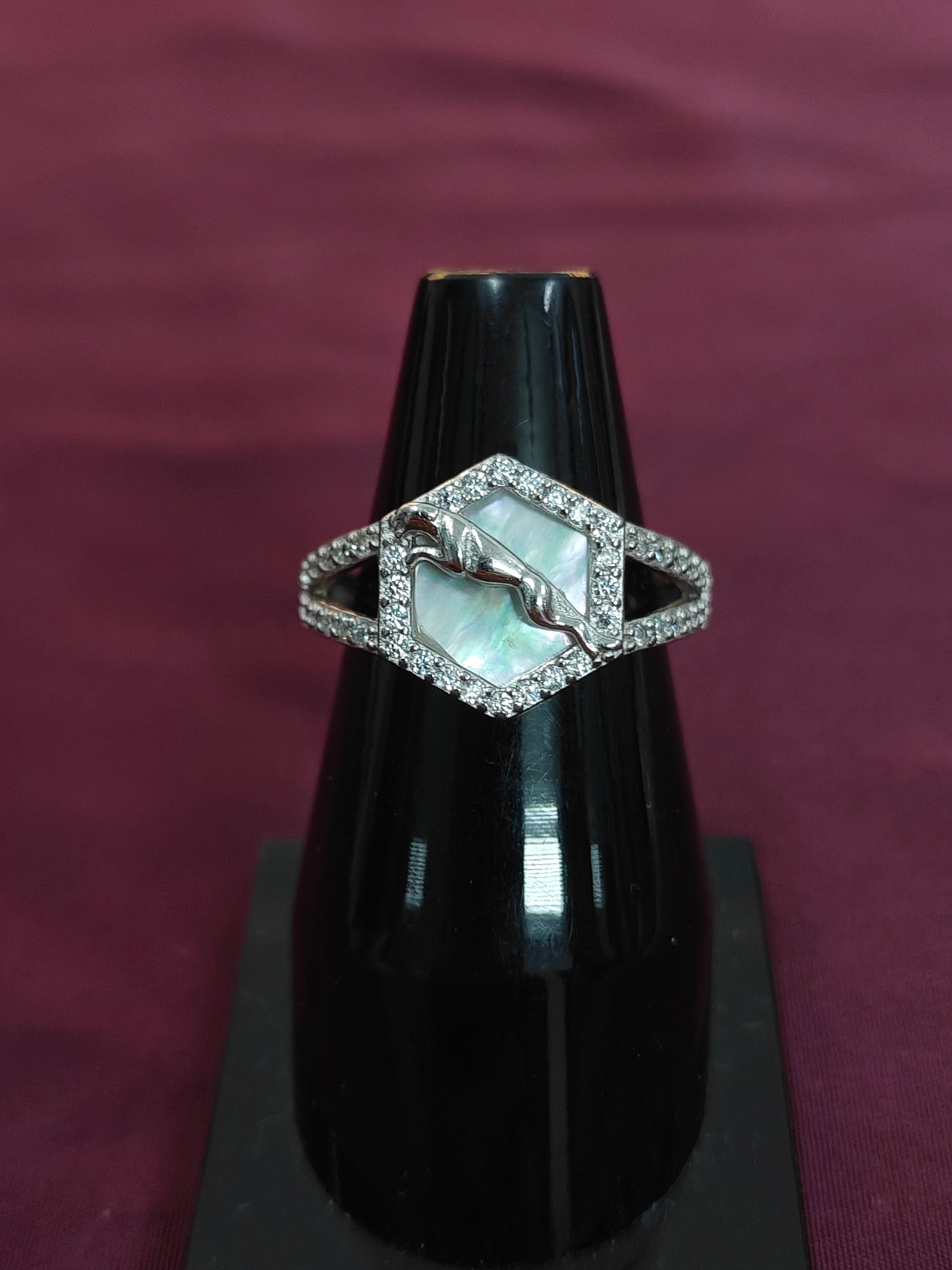 Silver ring with a central gemstone on a black stand against a purple background
