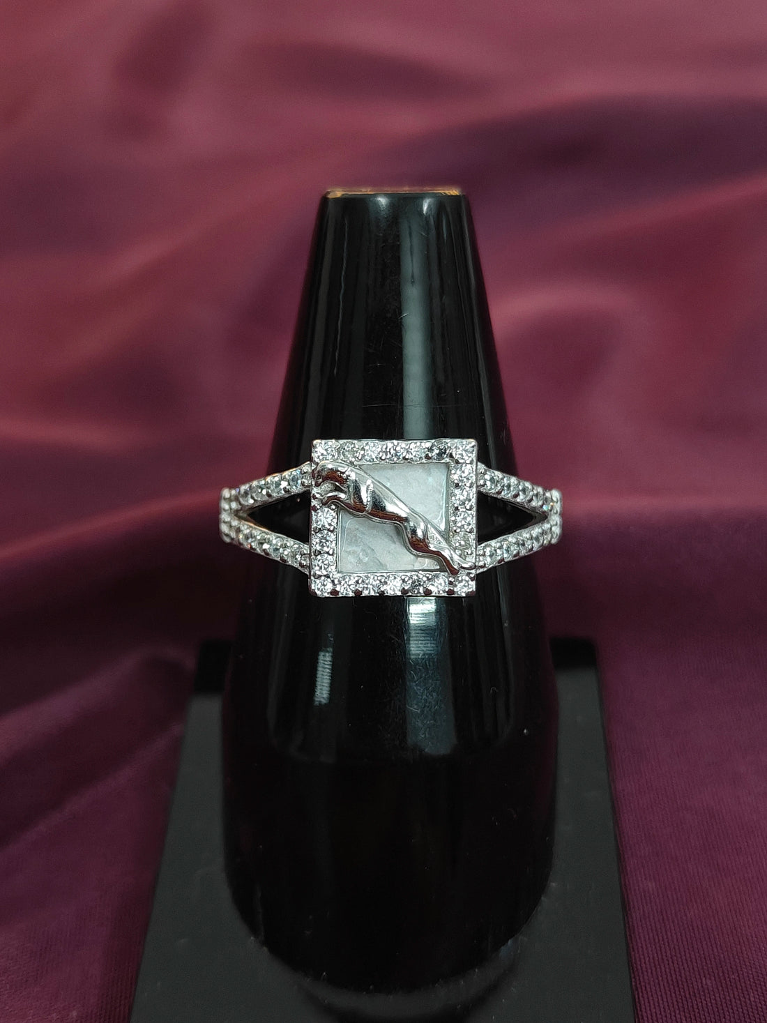 Silver ring with a diamond on a black stand against a purple fabric background