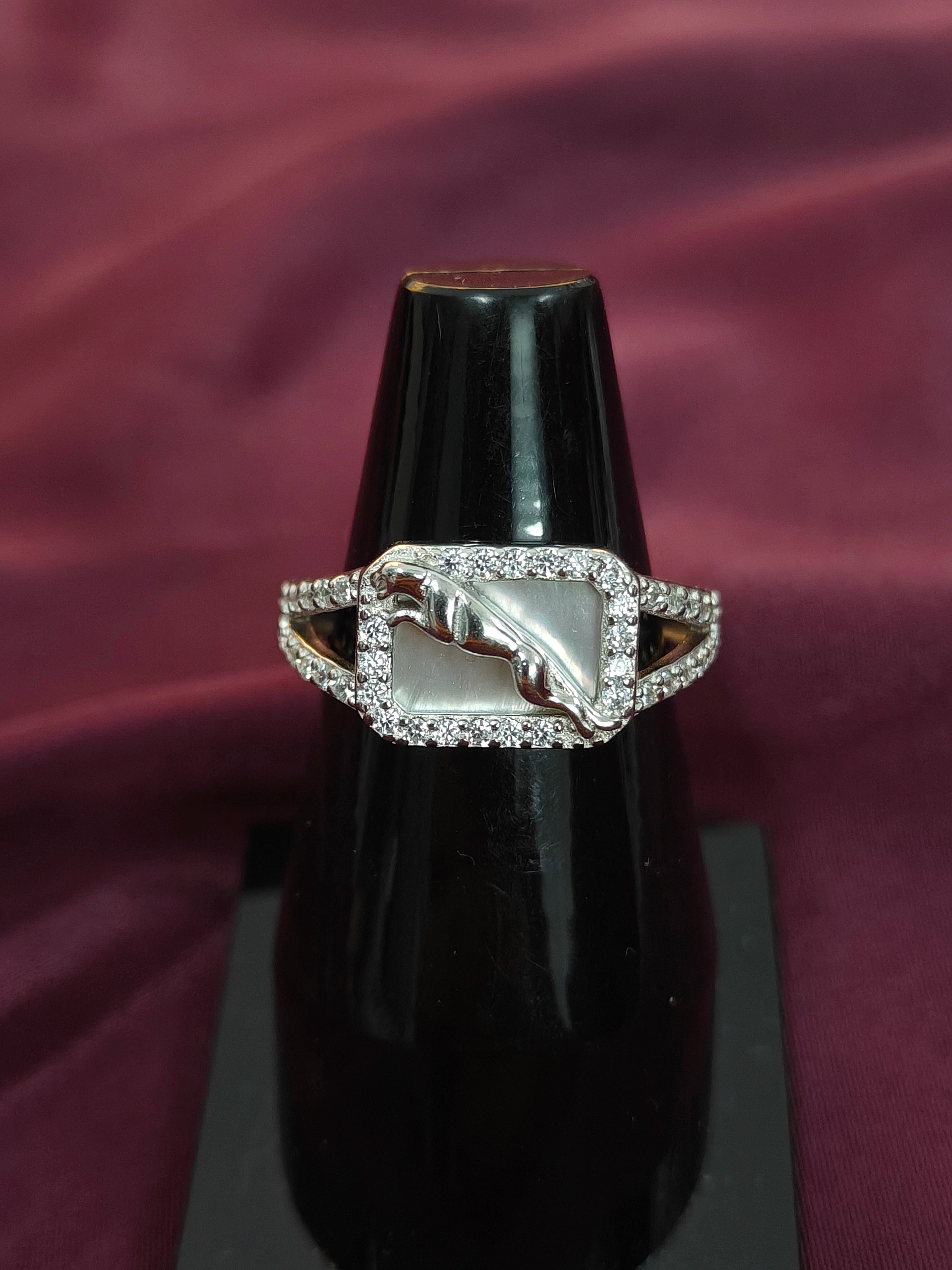 Silver ring with a central stone on a black stand against a purple fabric background