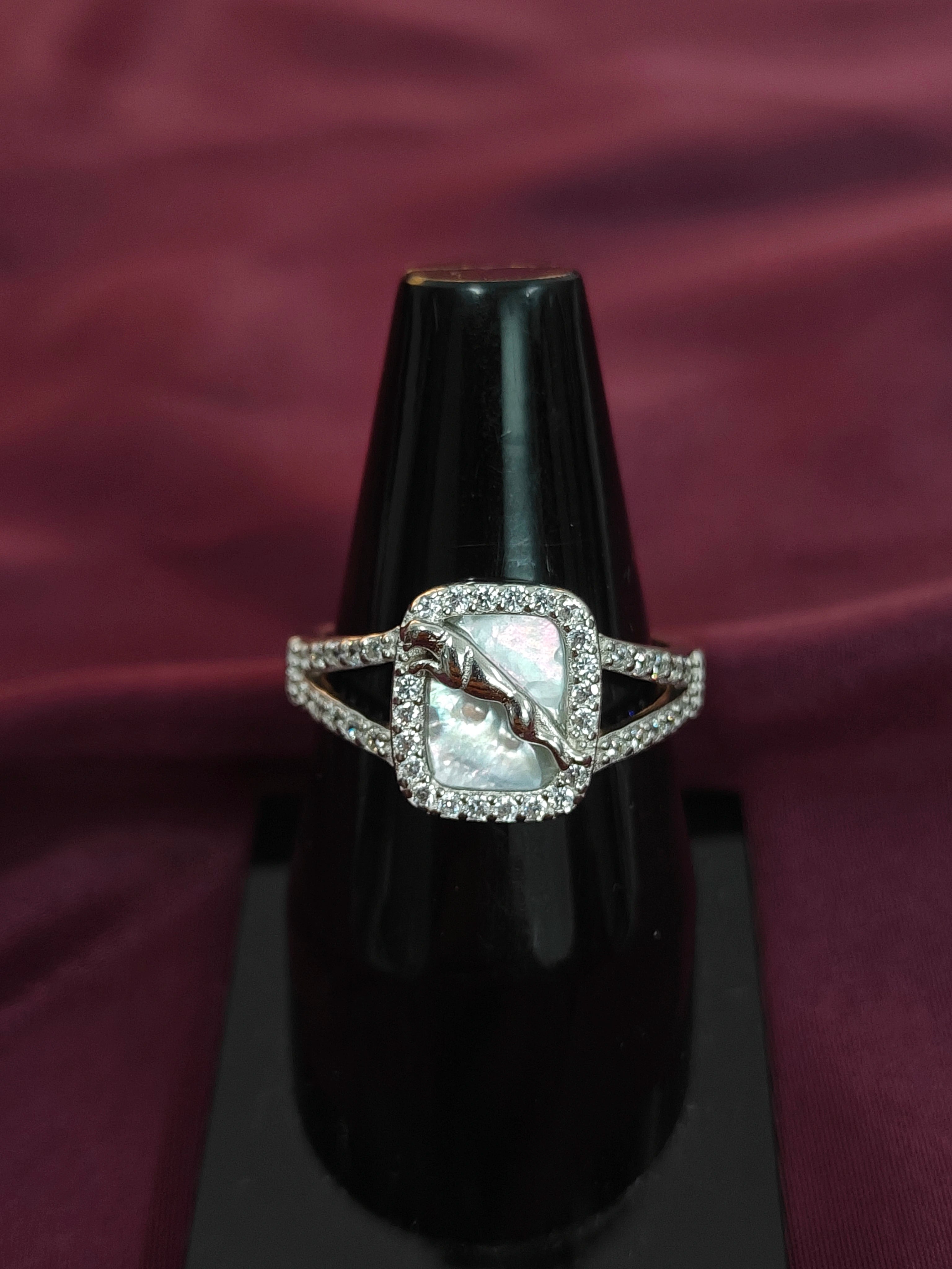 Silver ring with a central stone on a black stand against a purple fabric background