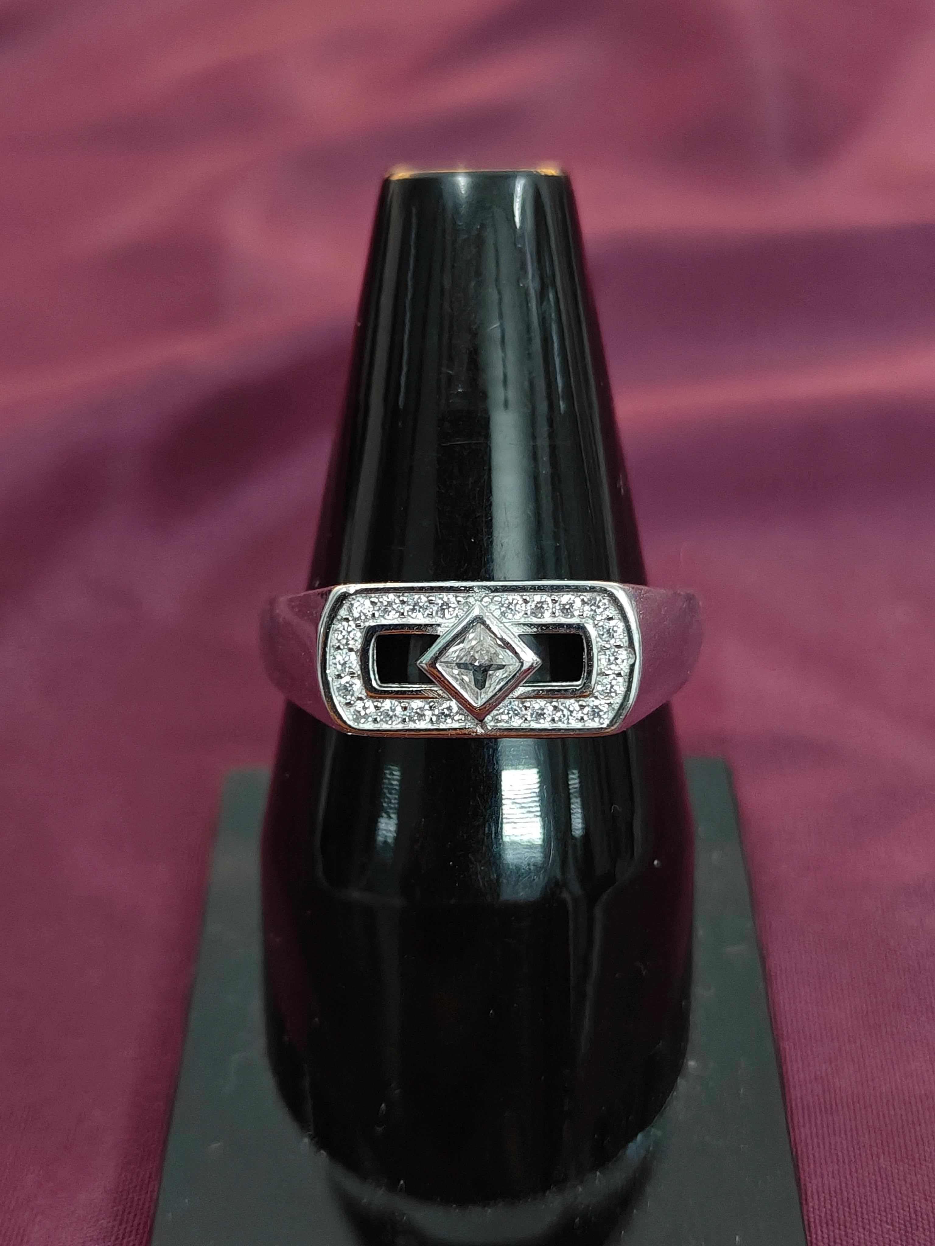 Silver ring with a diamond on a black stand against a purple fabric background