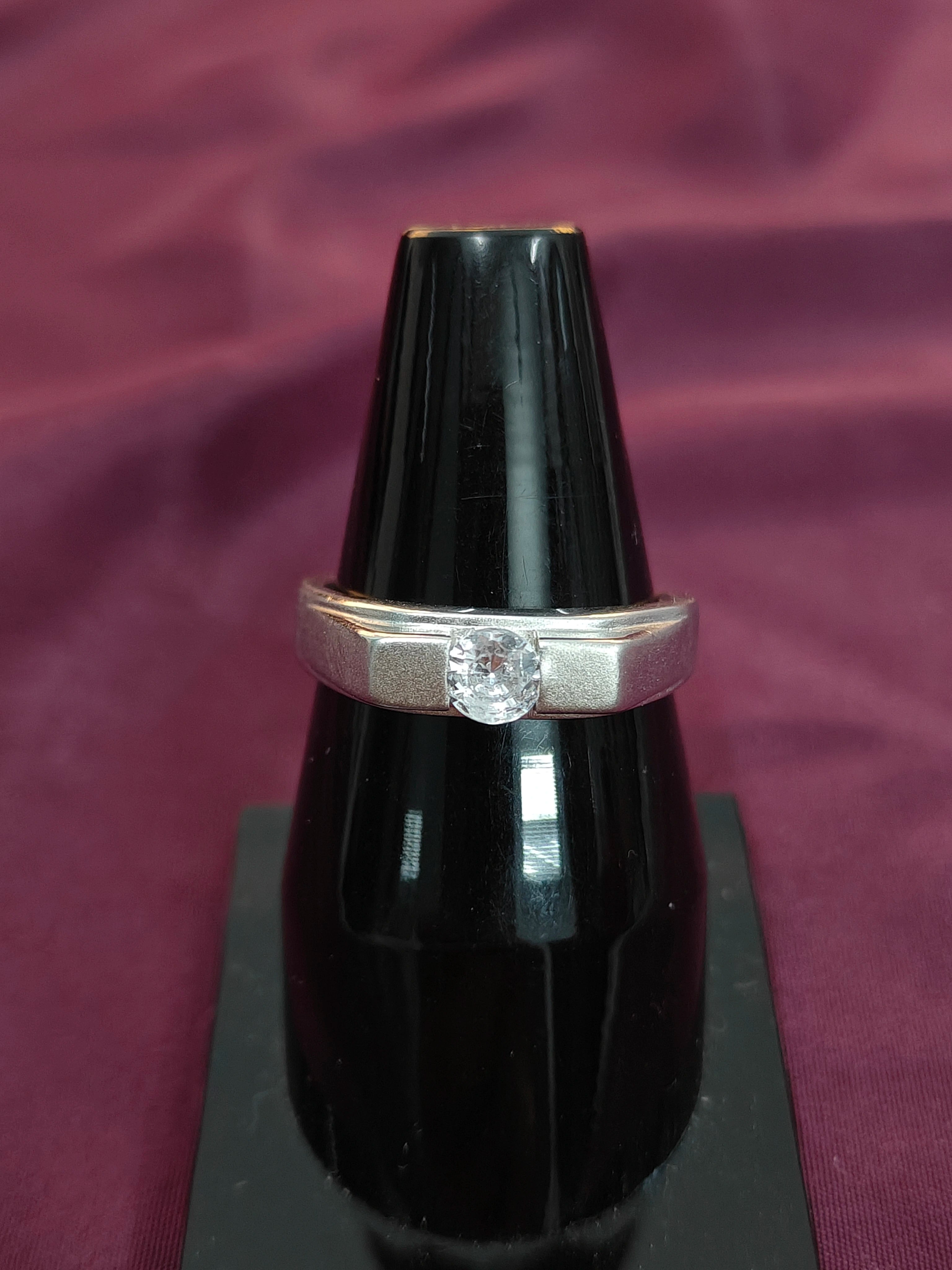 Silver ring with a diamond on a black lacquer surface against a purple fabric background