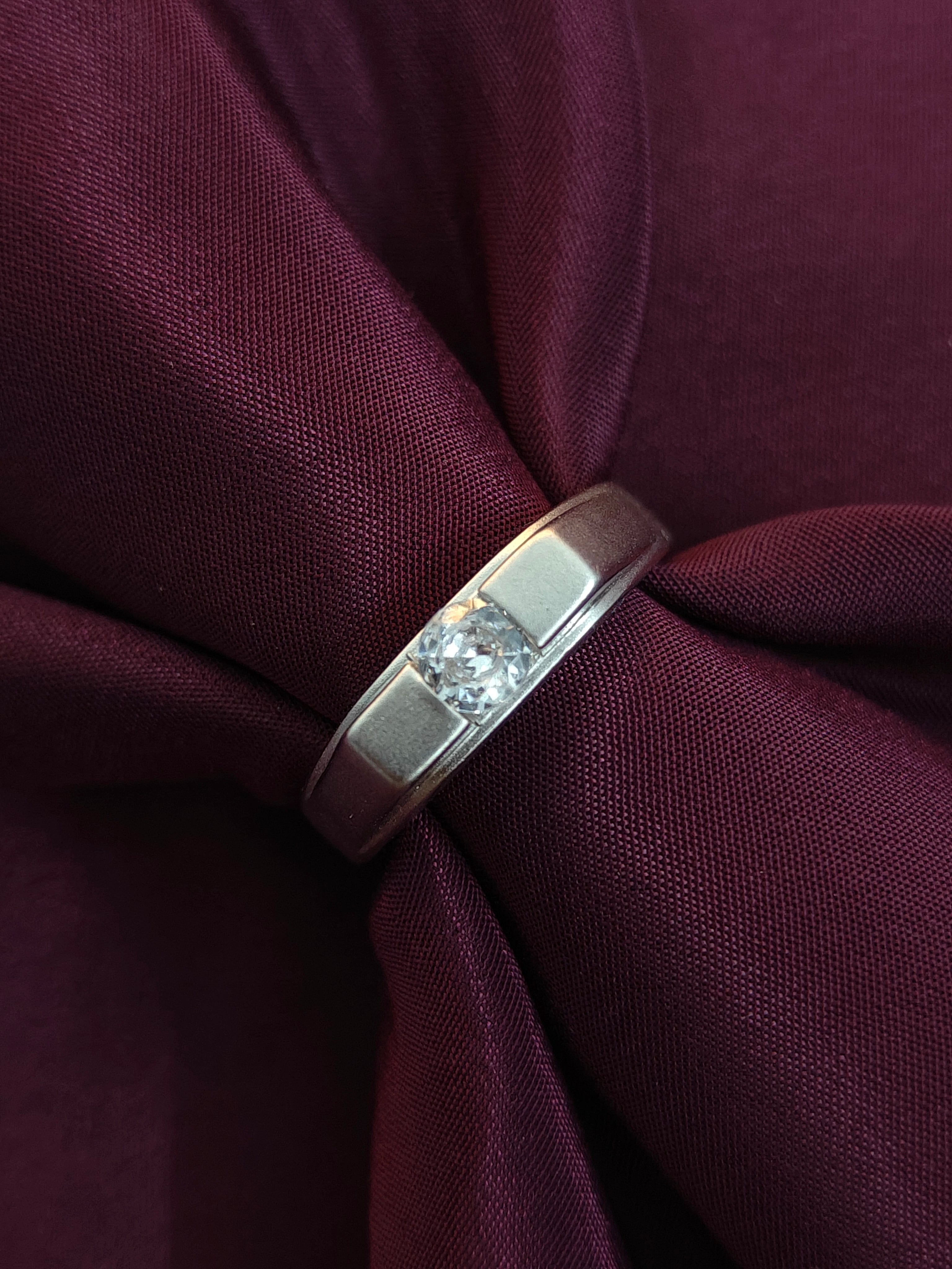 Silver ring with a diamond on a maroon fabric background
