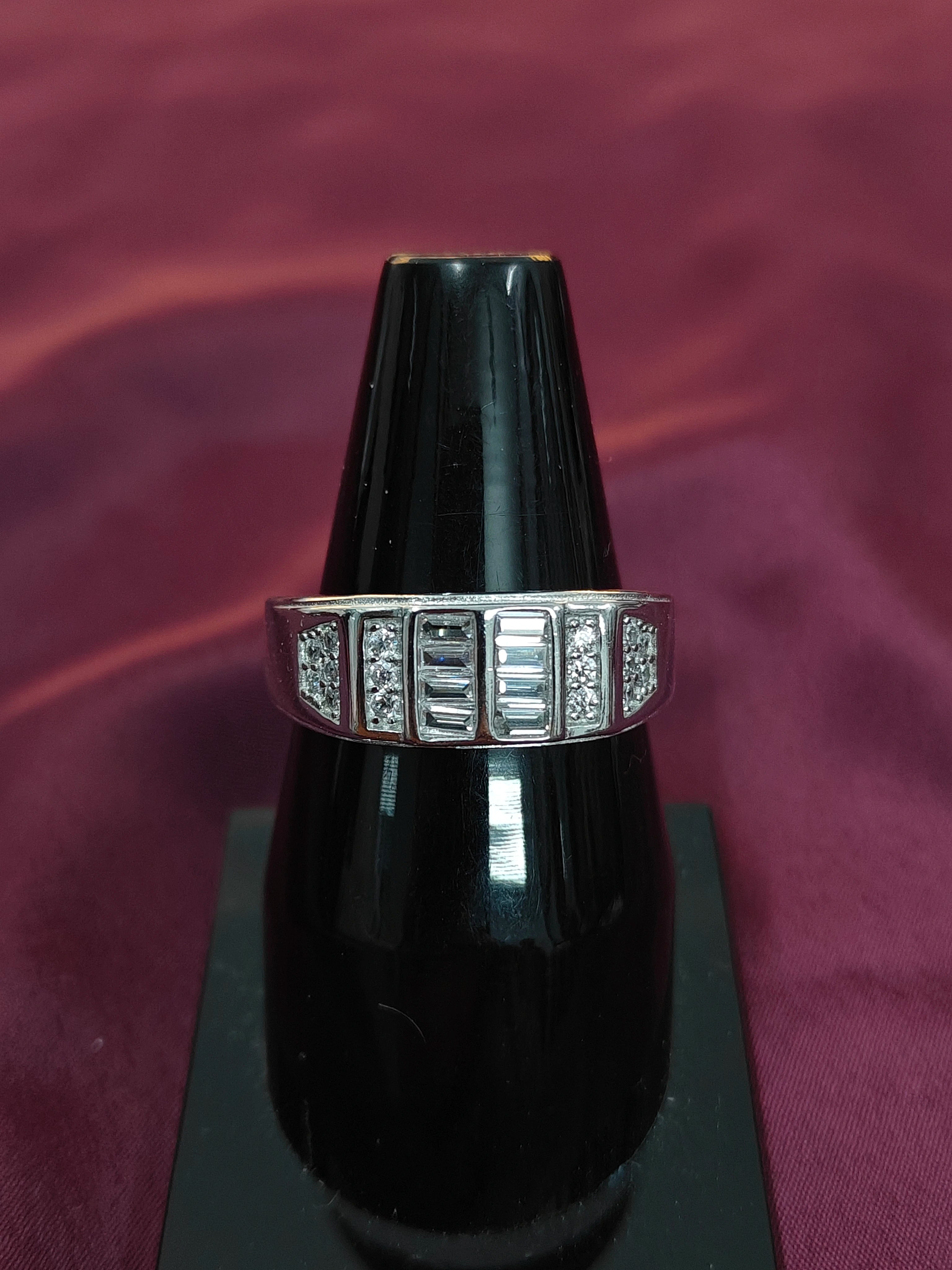 Silver ring with gemstones on a black stand against a purple background