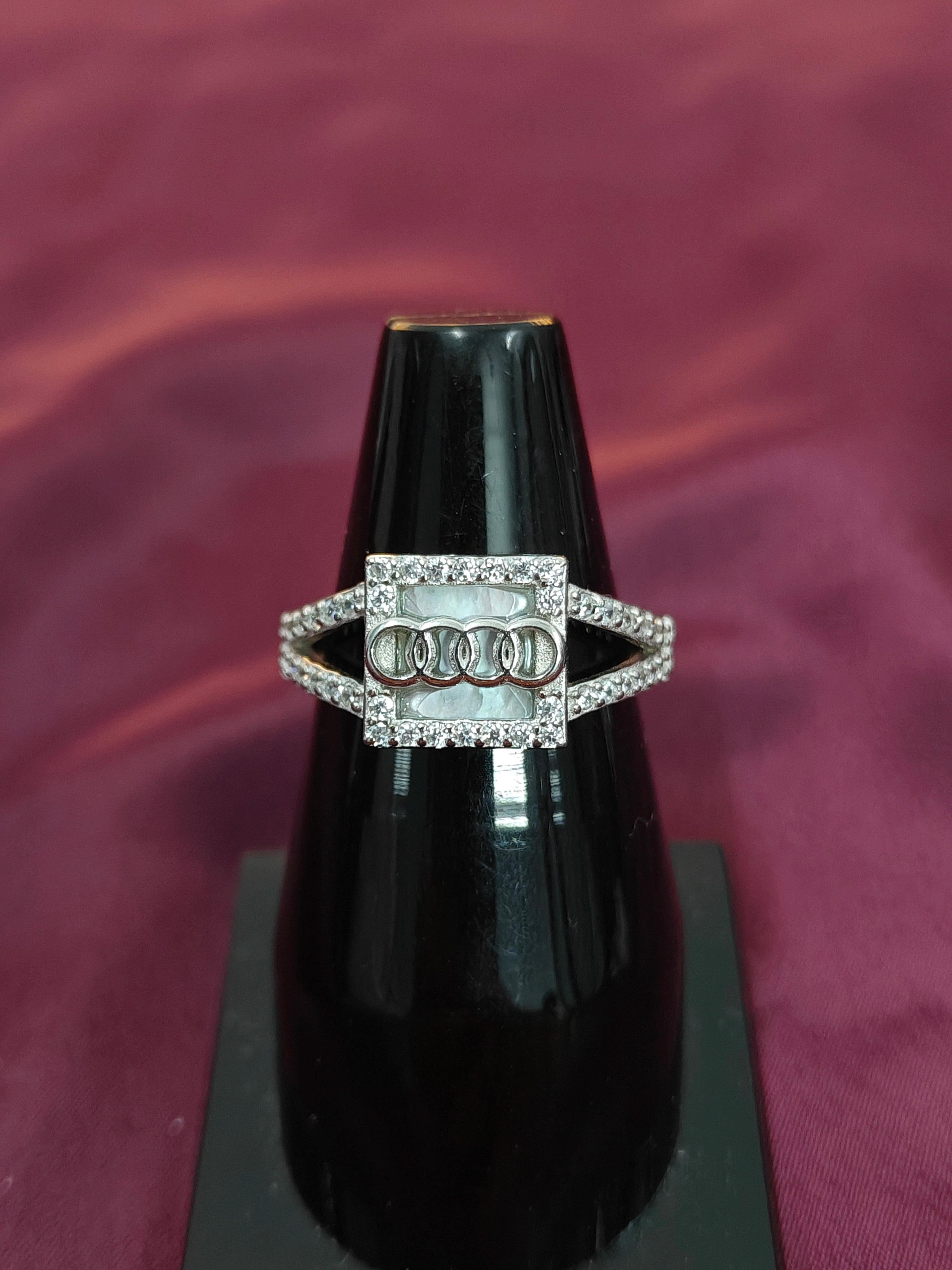 Silver ring with diamonds on a black stand against a maroon background