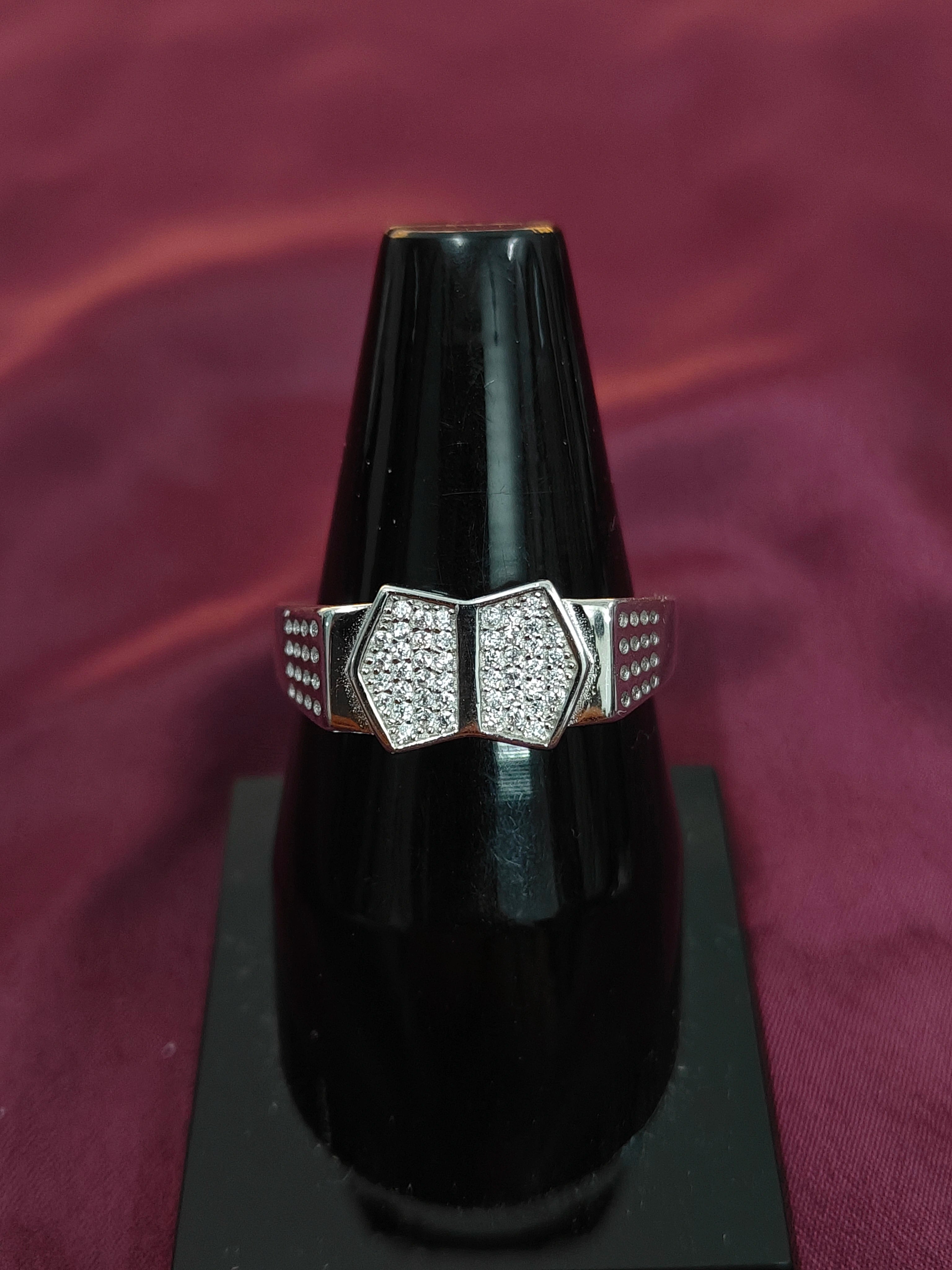 Silver ring with gemstones on a black stand against a purple background