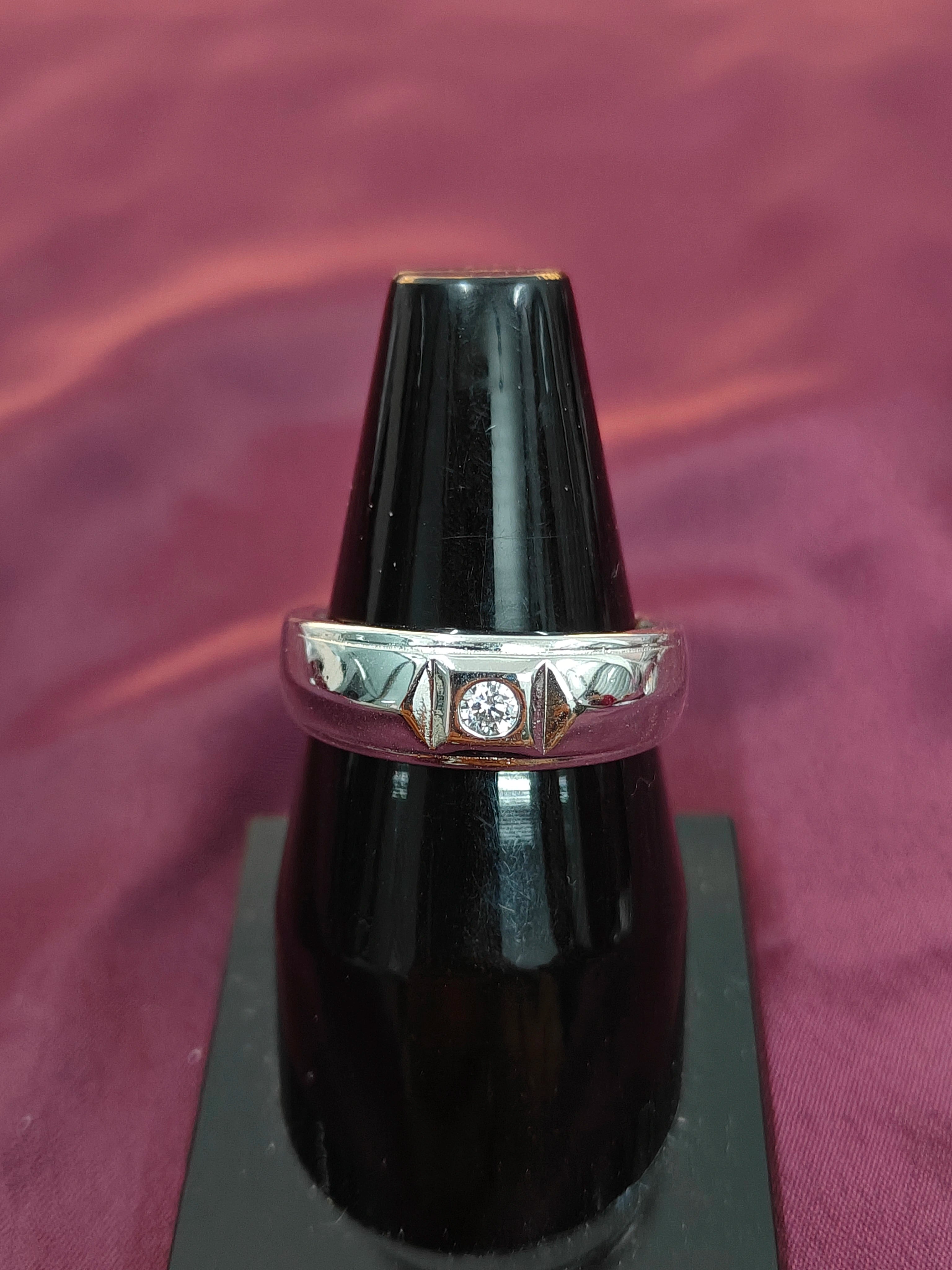 Silver ring with a diamond on a black stand against a purple fabric background