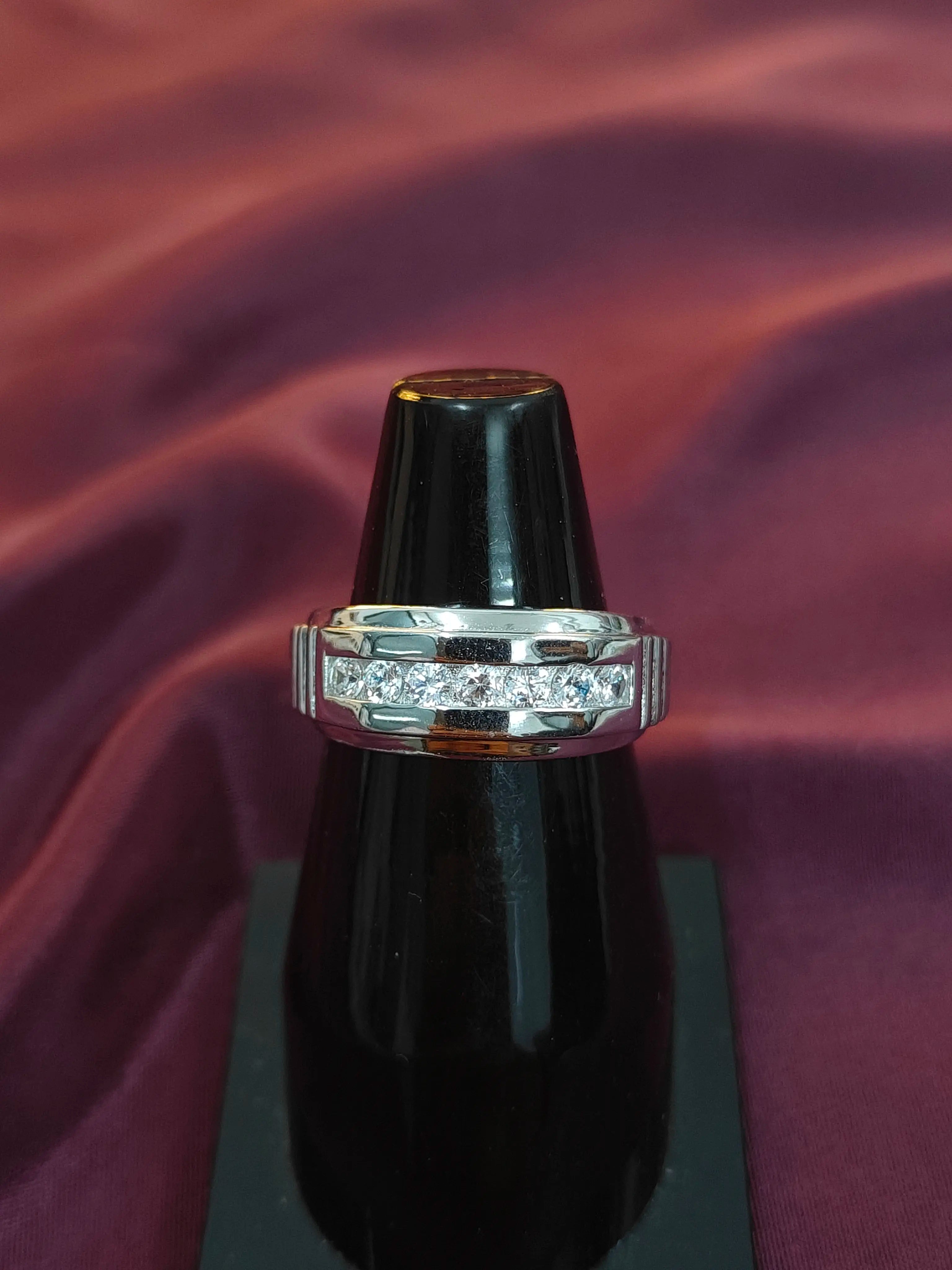 Silver ring with diamonds on a black stand against a purple fabric background