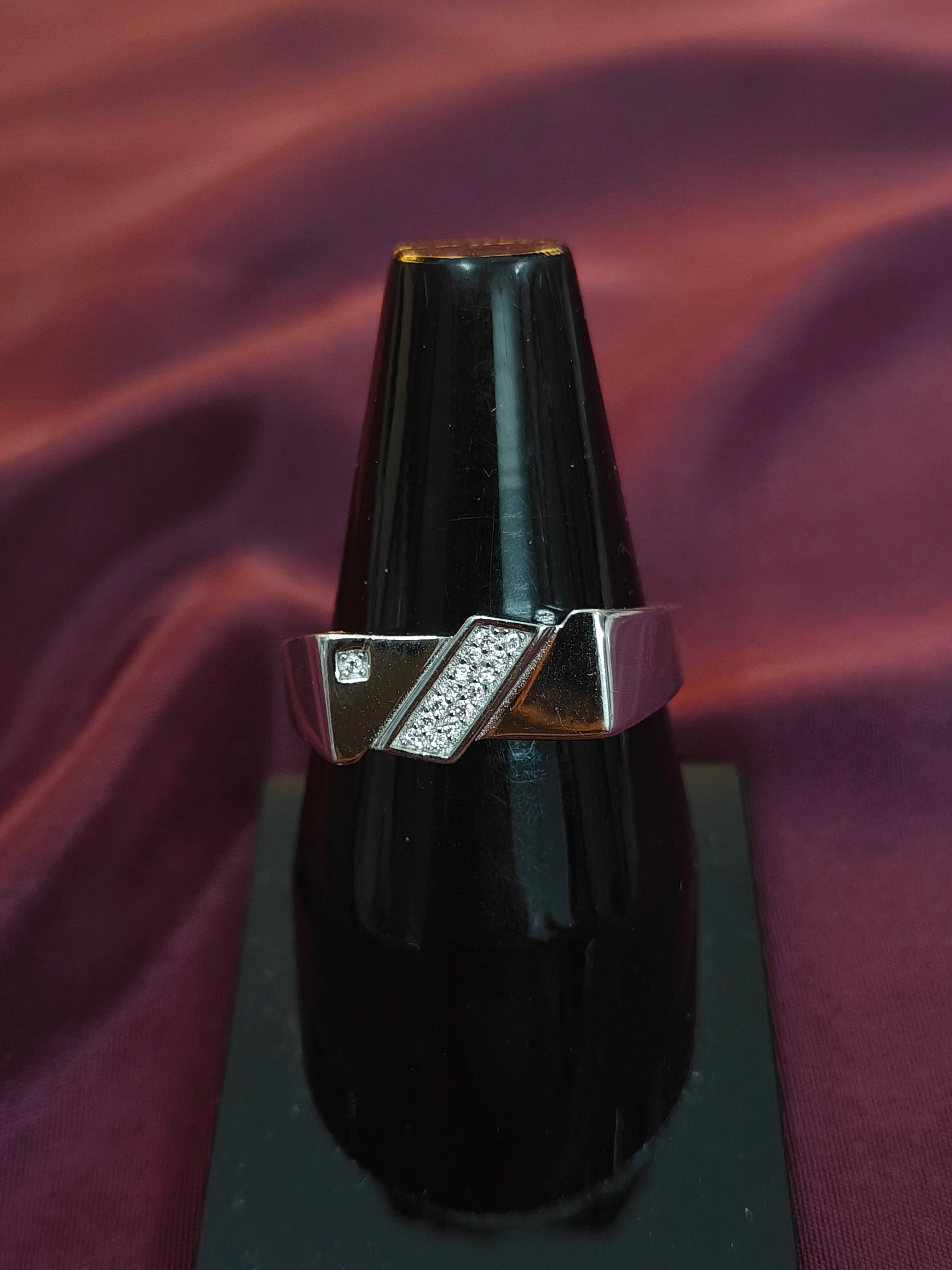 Silver ring with a diamond on a black stand against a purple fabric background