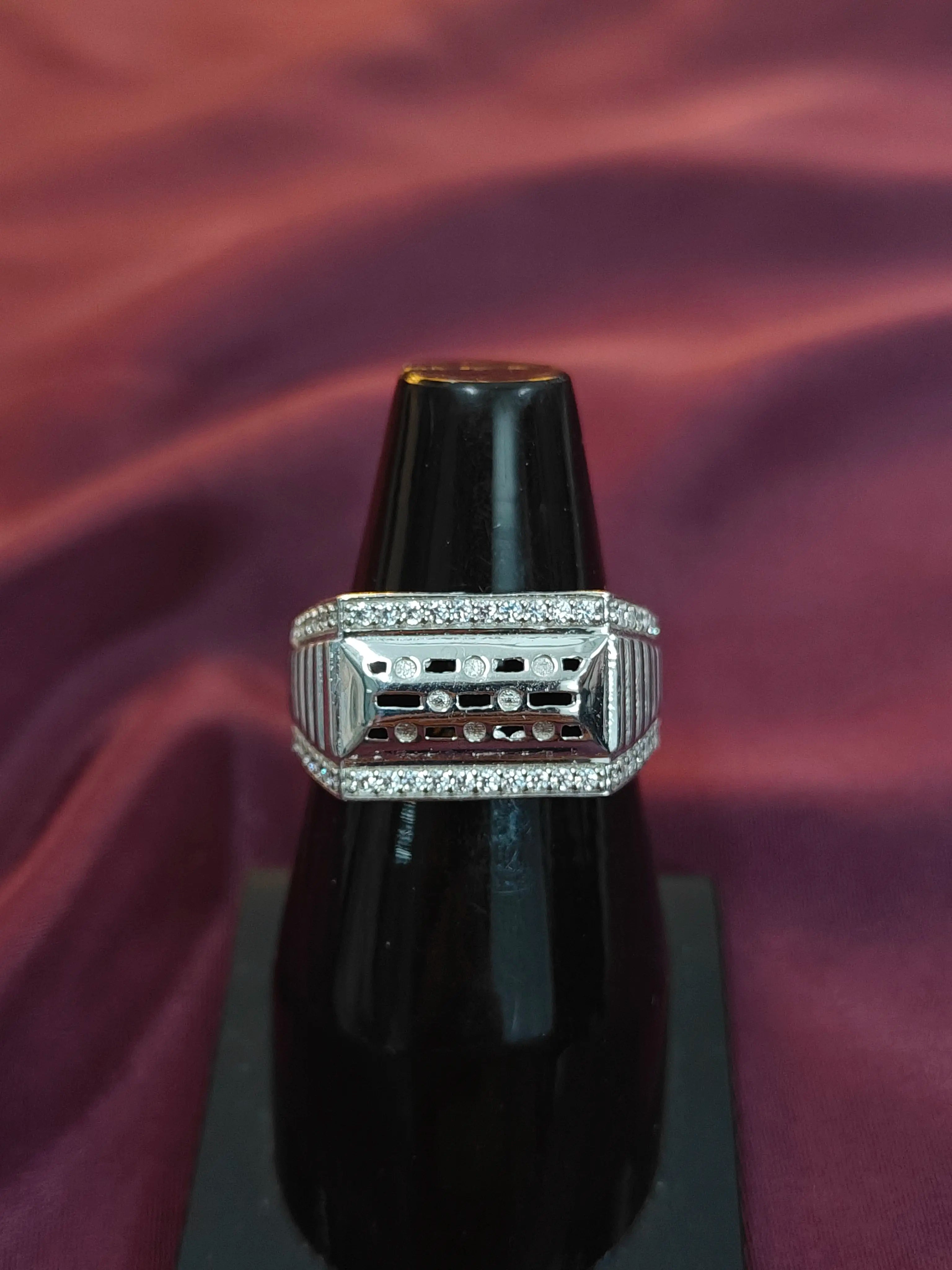 Silver ring with gemstones on a black stand against a purple fabric background