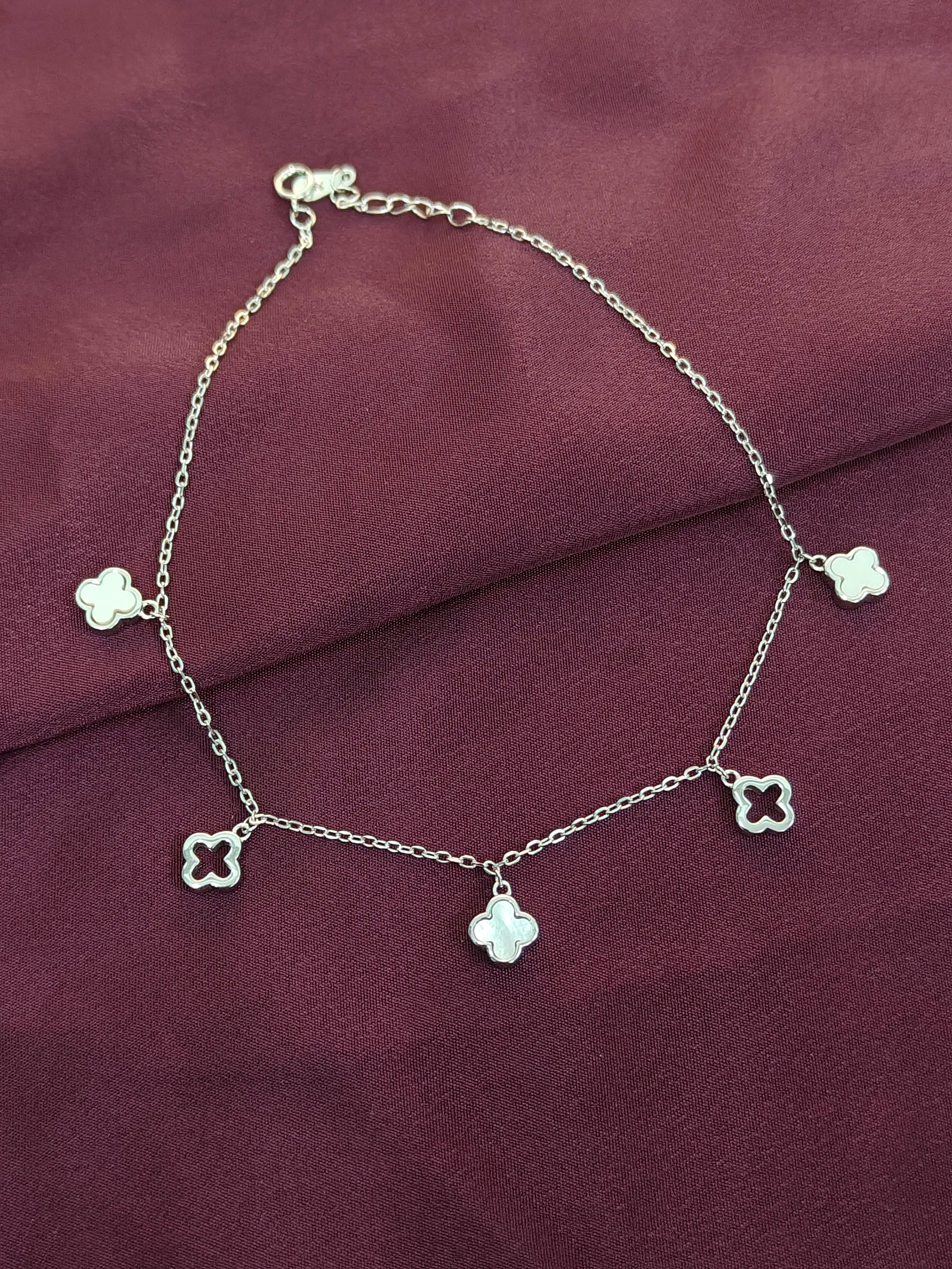 Silver anklet with clover-shaped charms on a purple fabric background