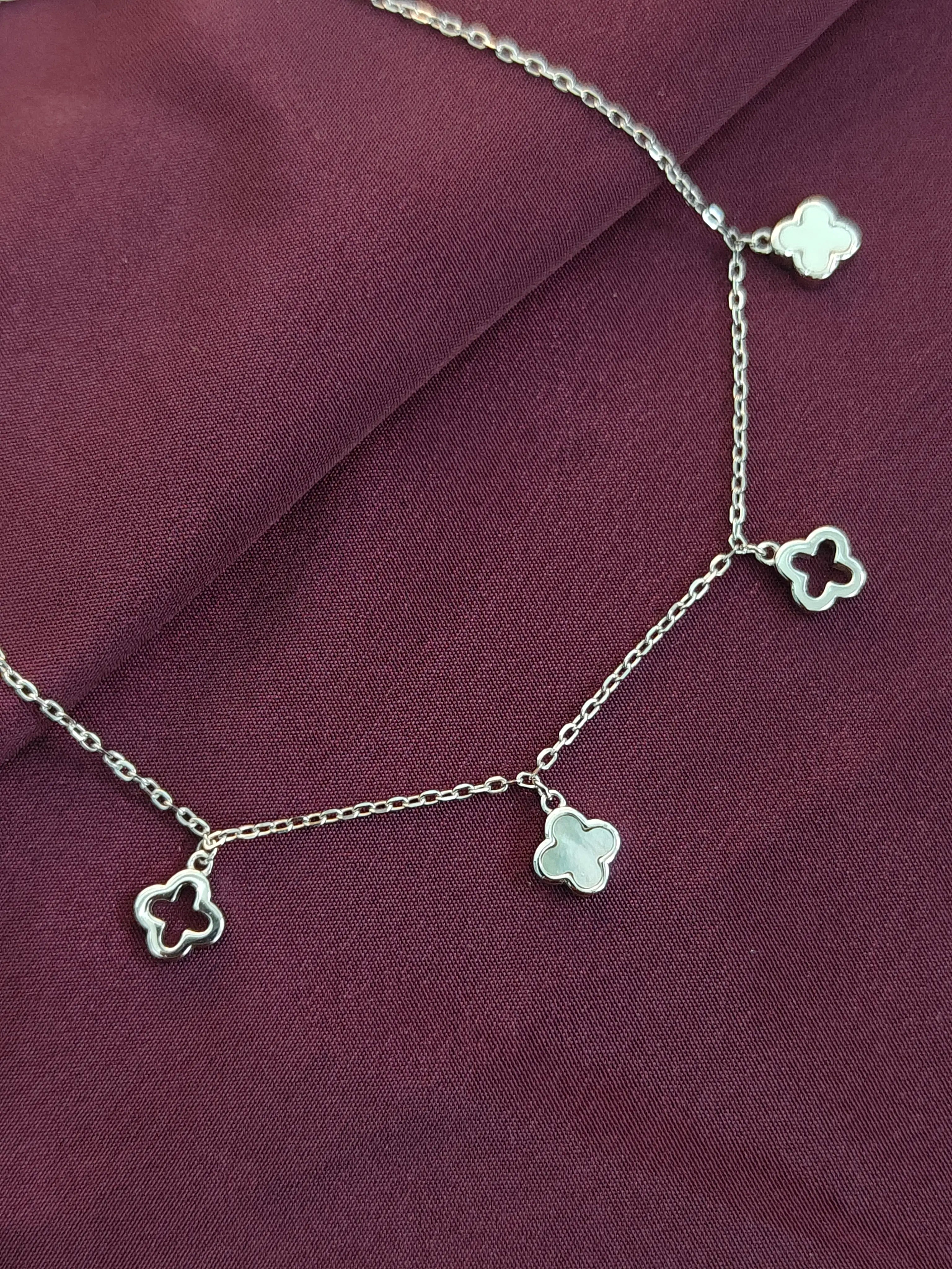 Silver necklace with clover-shaped charms on a purple fabric background