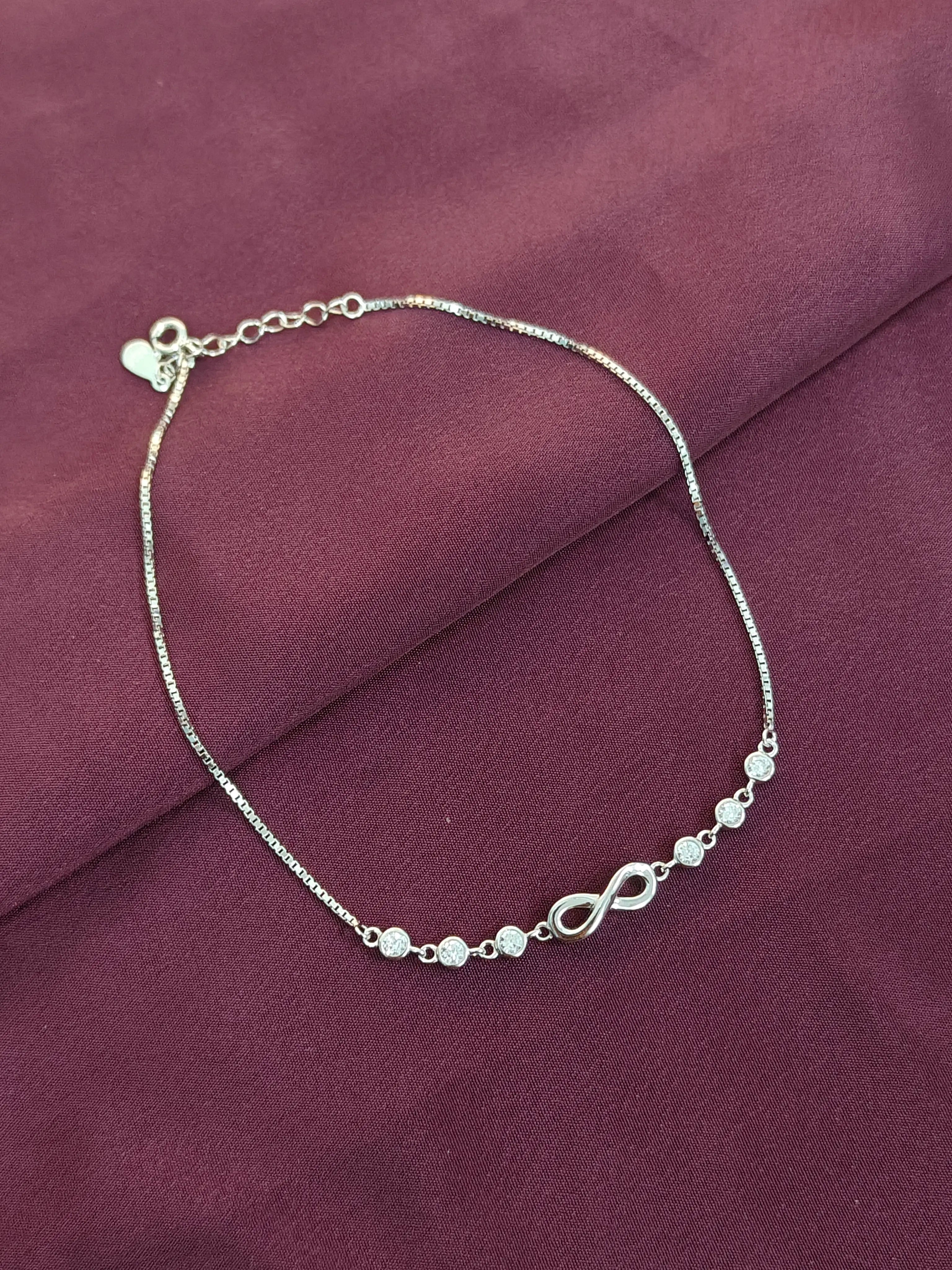 Silver bracelet with infinity symbols on a purple fabric background
