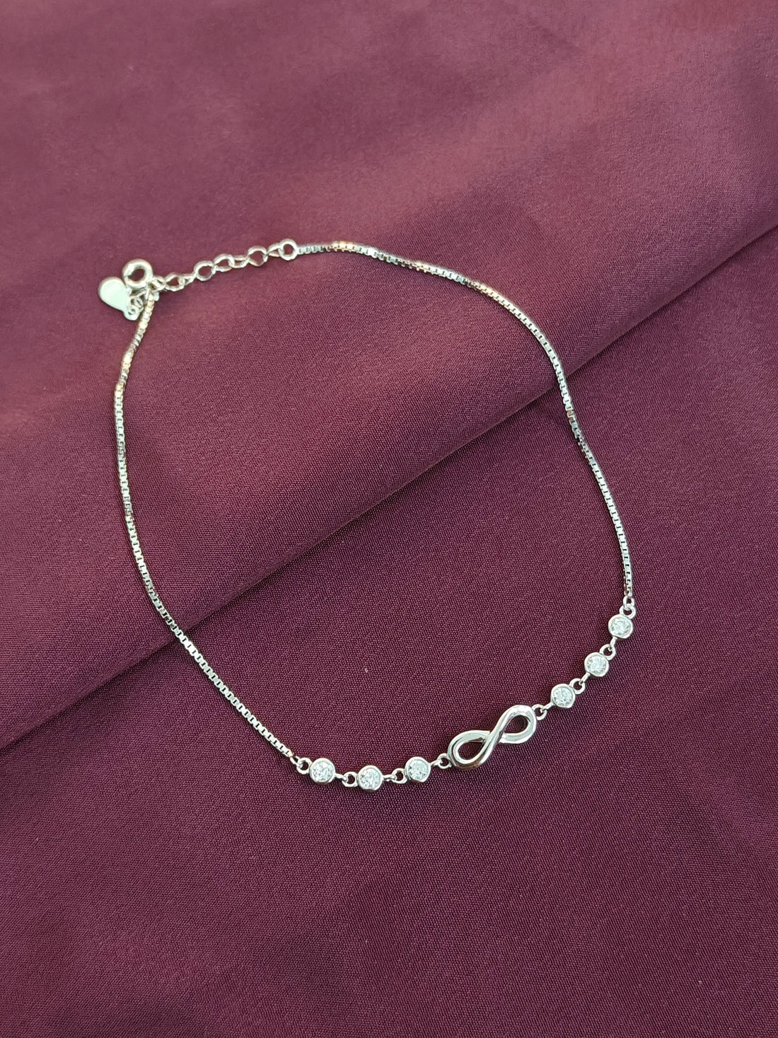 Silver bracelet with infinity symbols on a purple fabric background