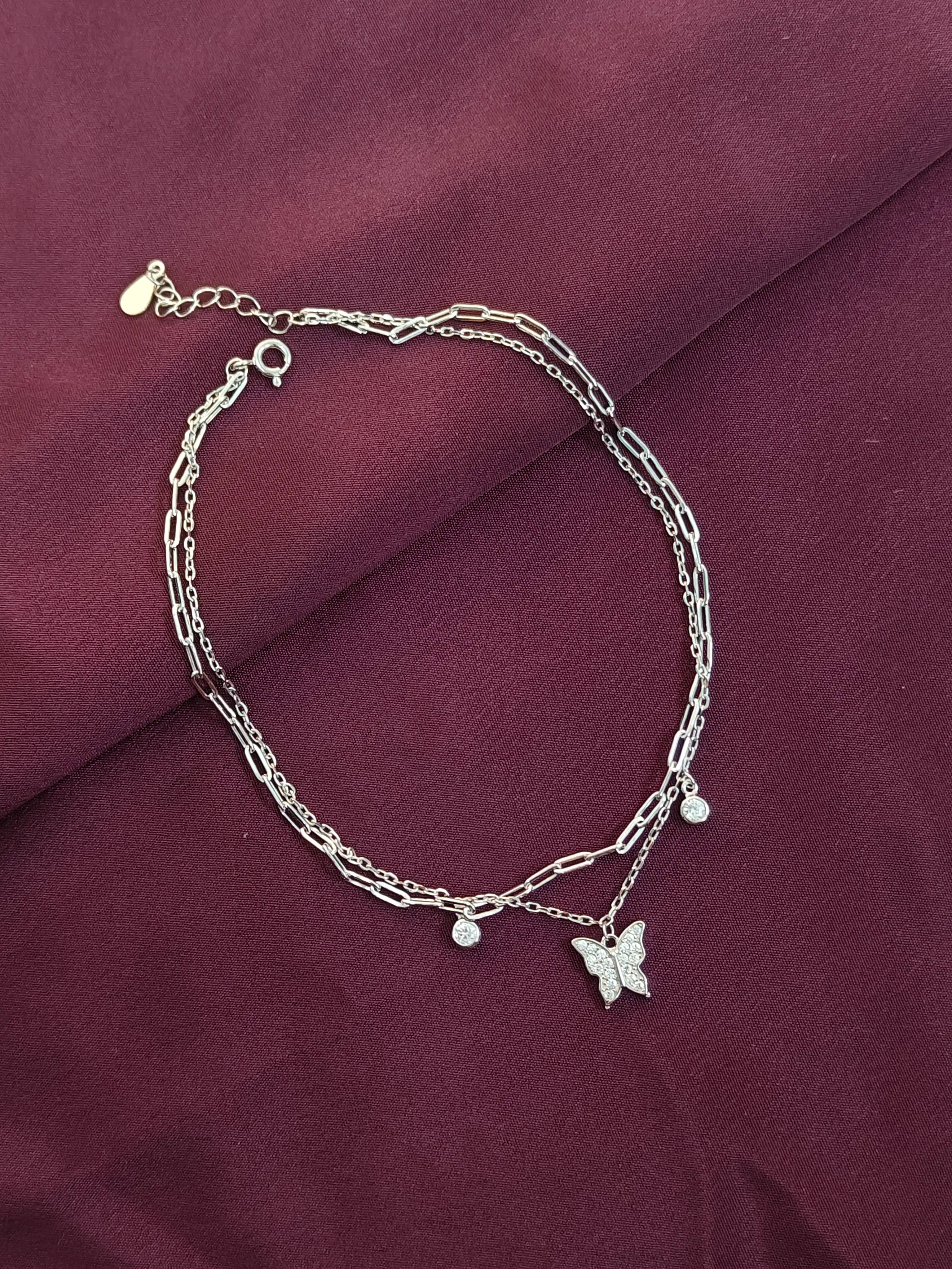Silver bracelet with butterfly charm on a maroon fabric background