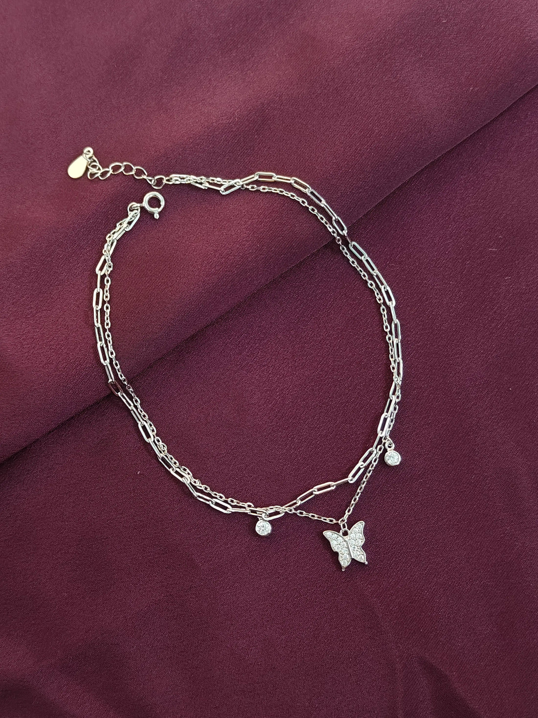 Silver bracelet with butterfly charm on a maroon fabric background