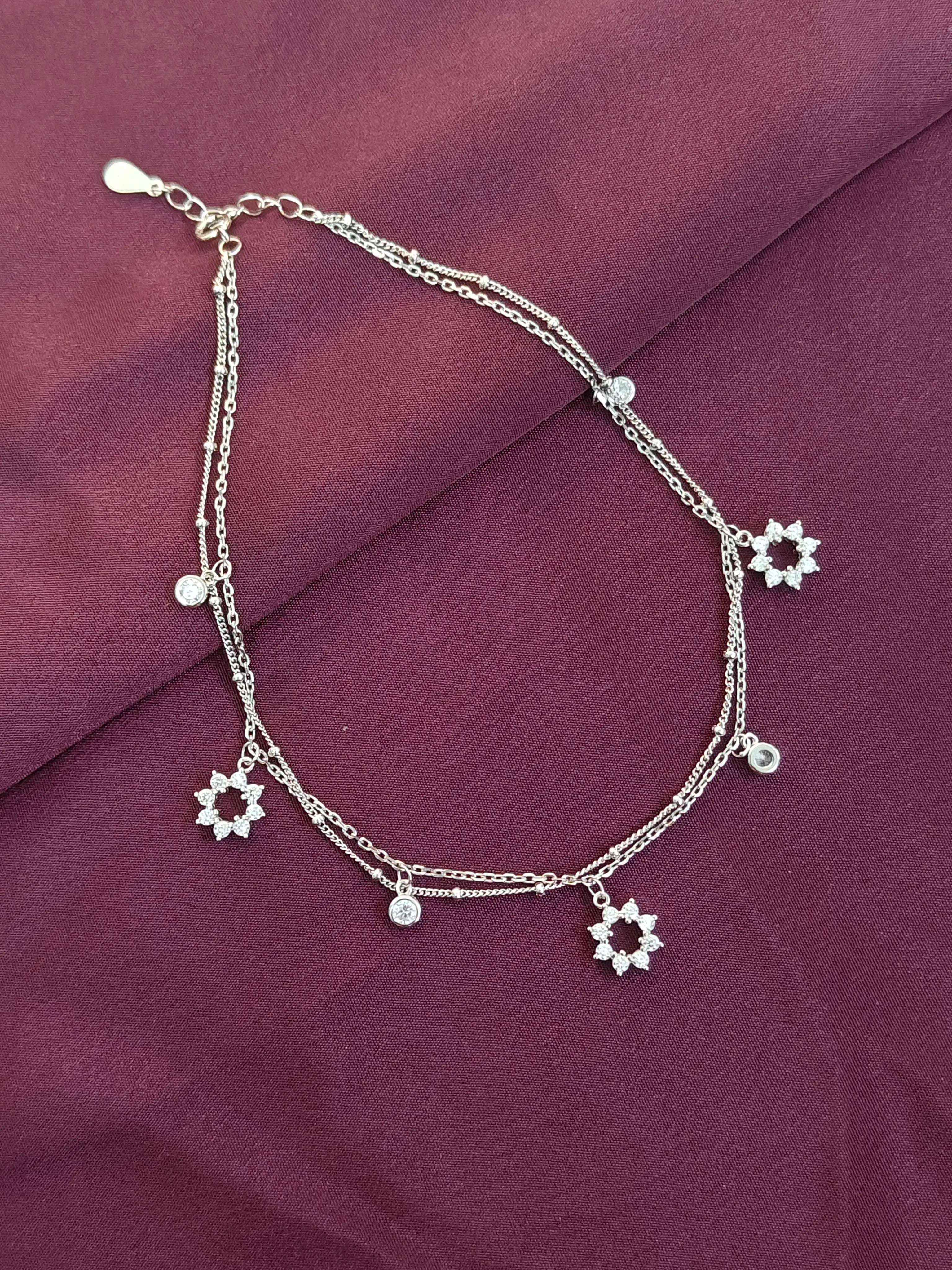 Silver anklet with star-shaped charms on a purple fabric background