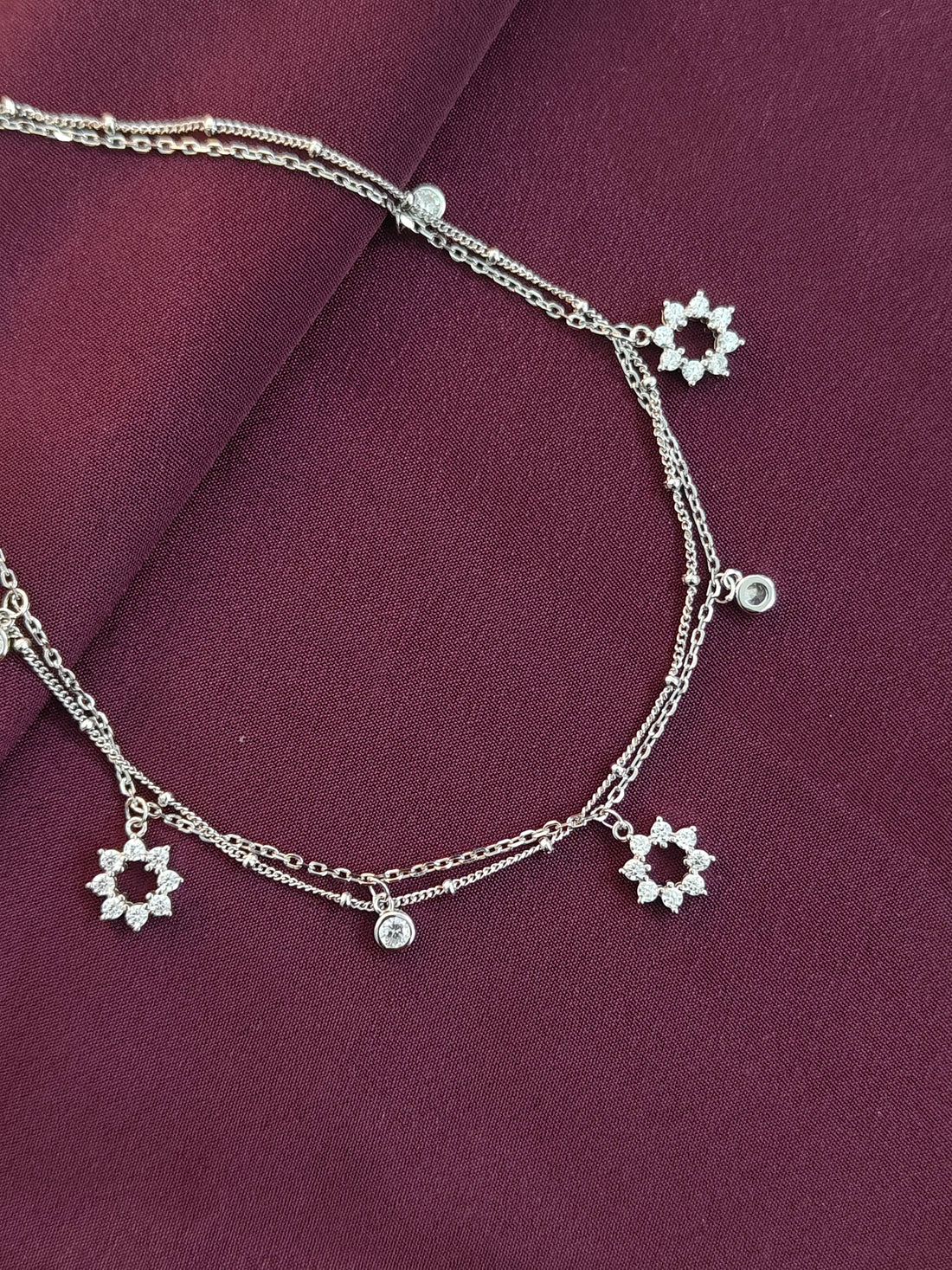 Silver anklets with floral charms on a purple fabric background