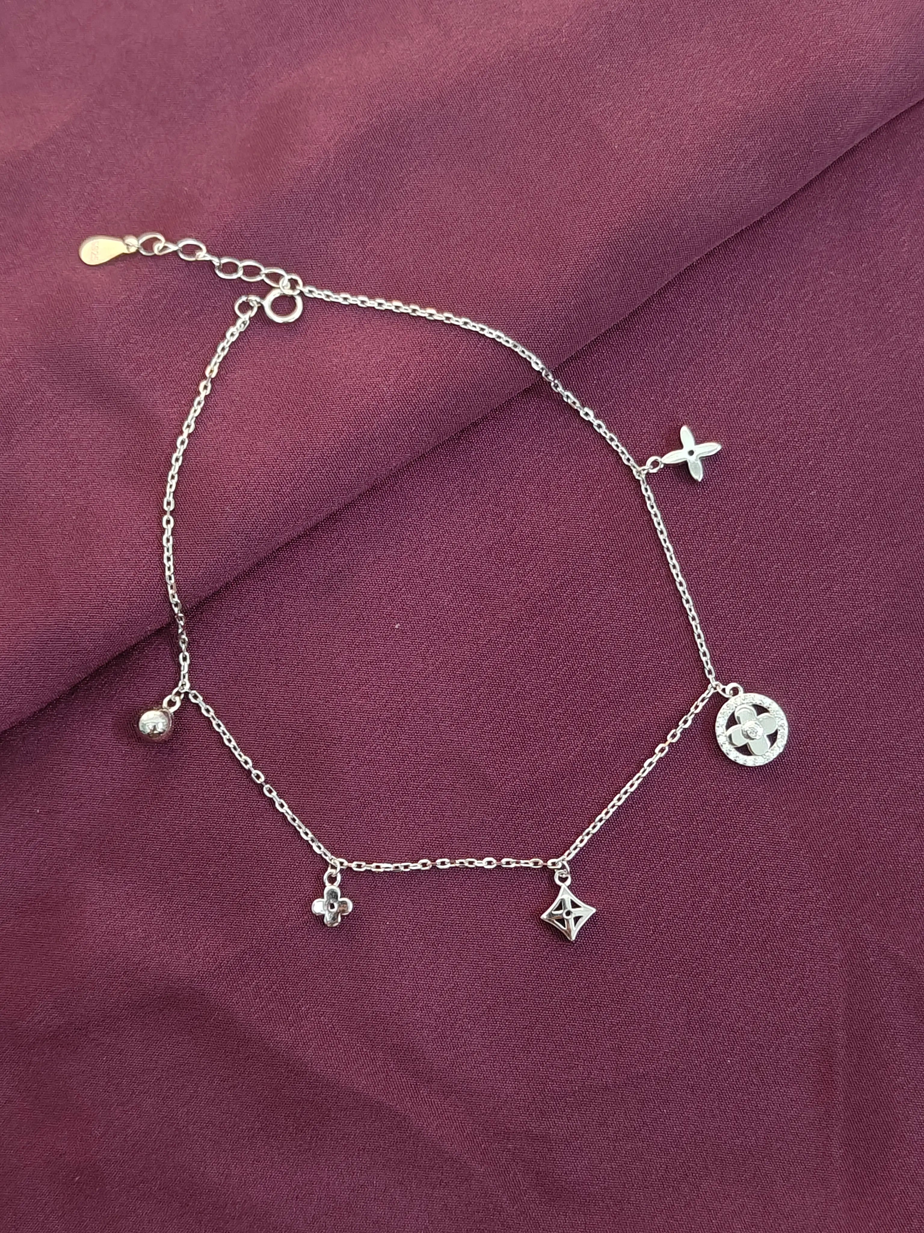 Silver anklet with charms on a purple fabric background