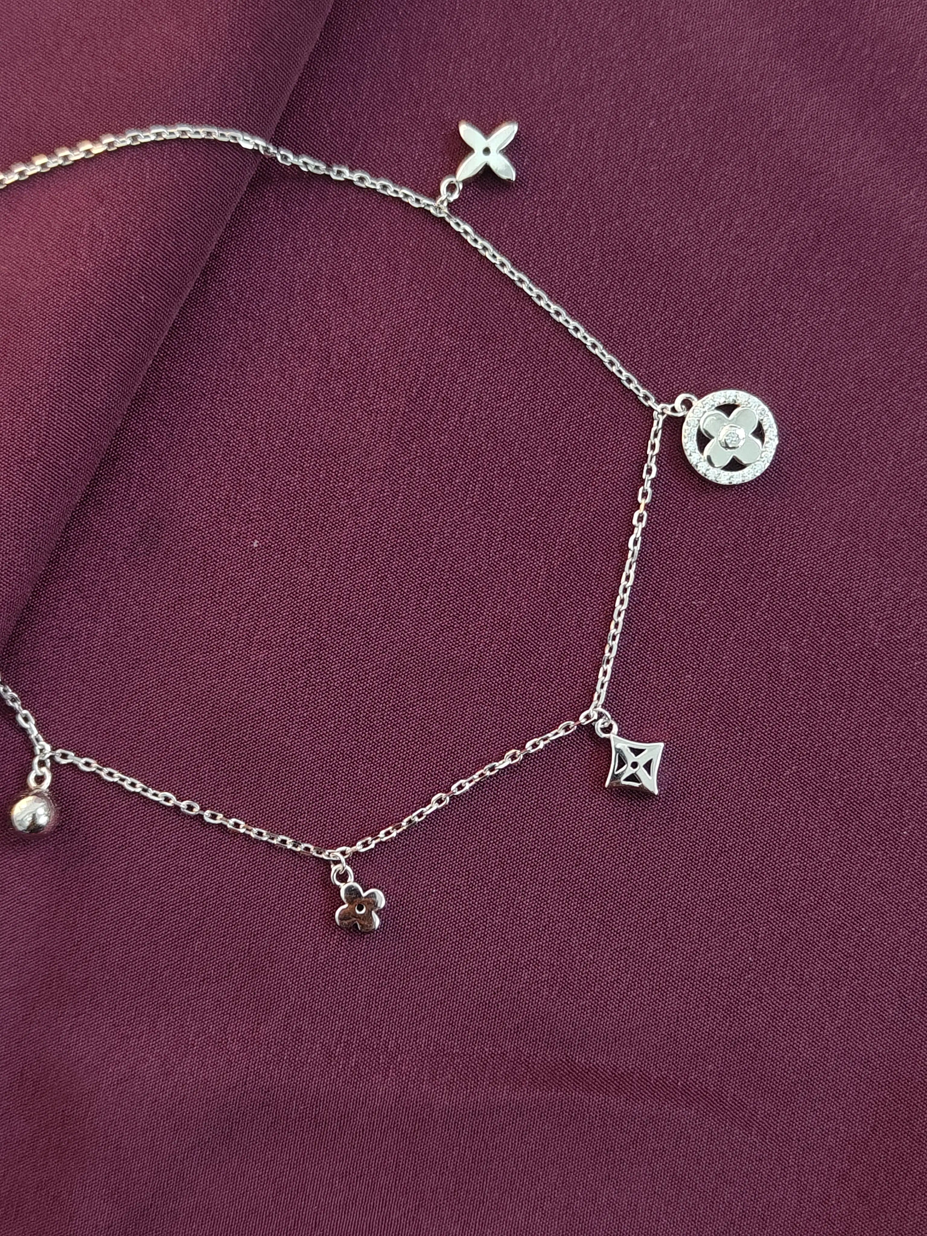 Silver anklet with charms on a maroon fabric background