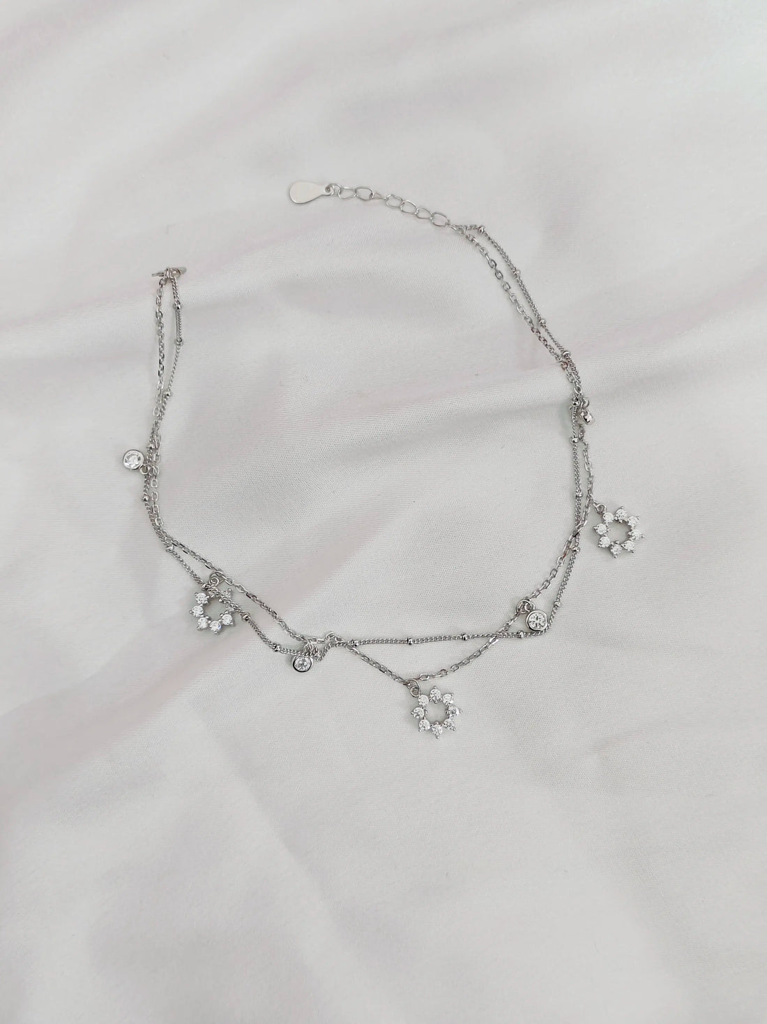 Silver necklace with floral designs on a light gray background