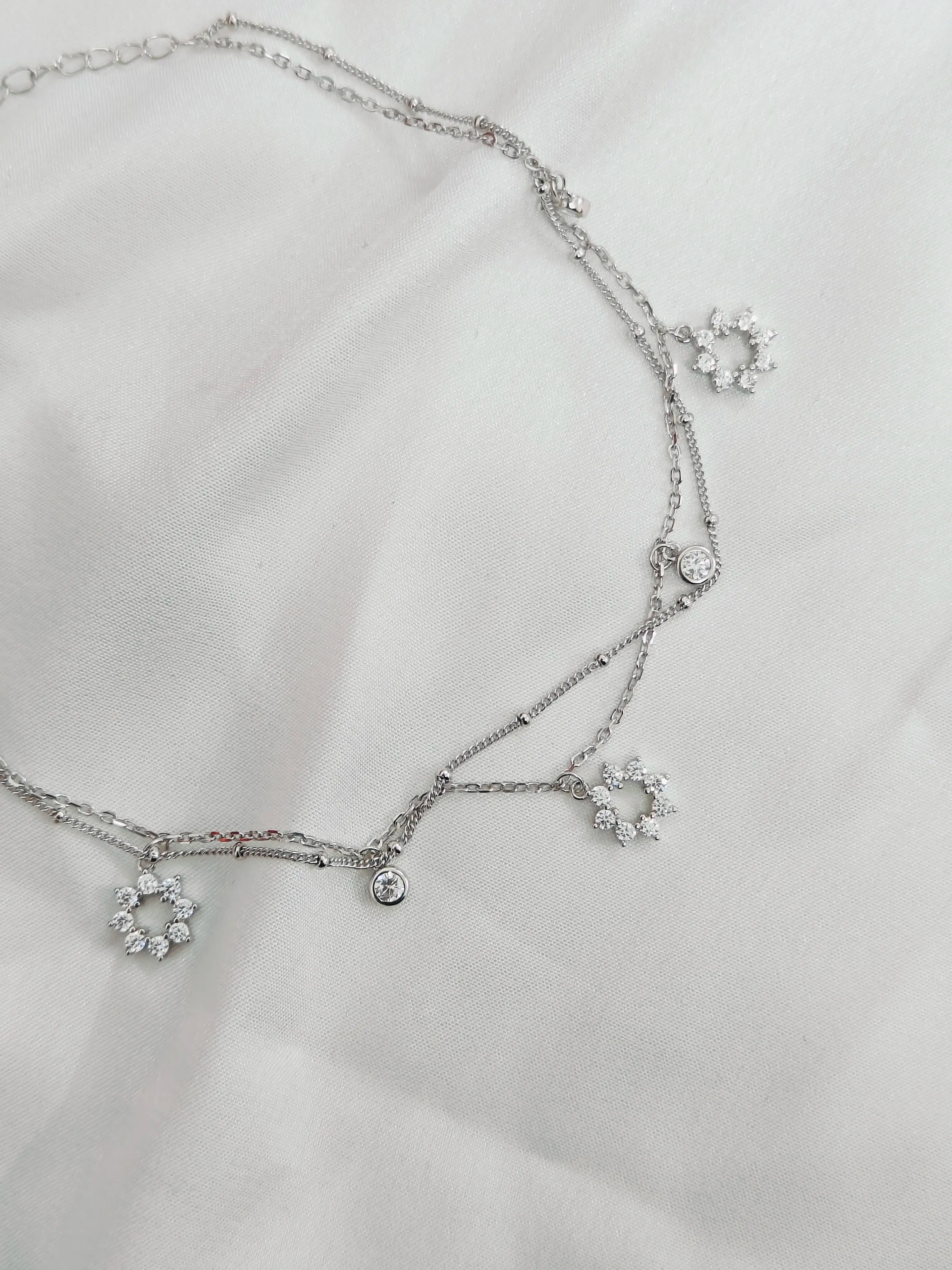 Silver necklace with floral pendants on a light gray background