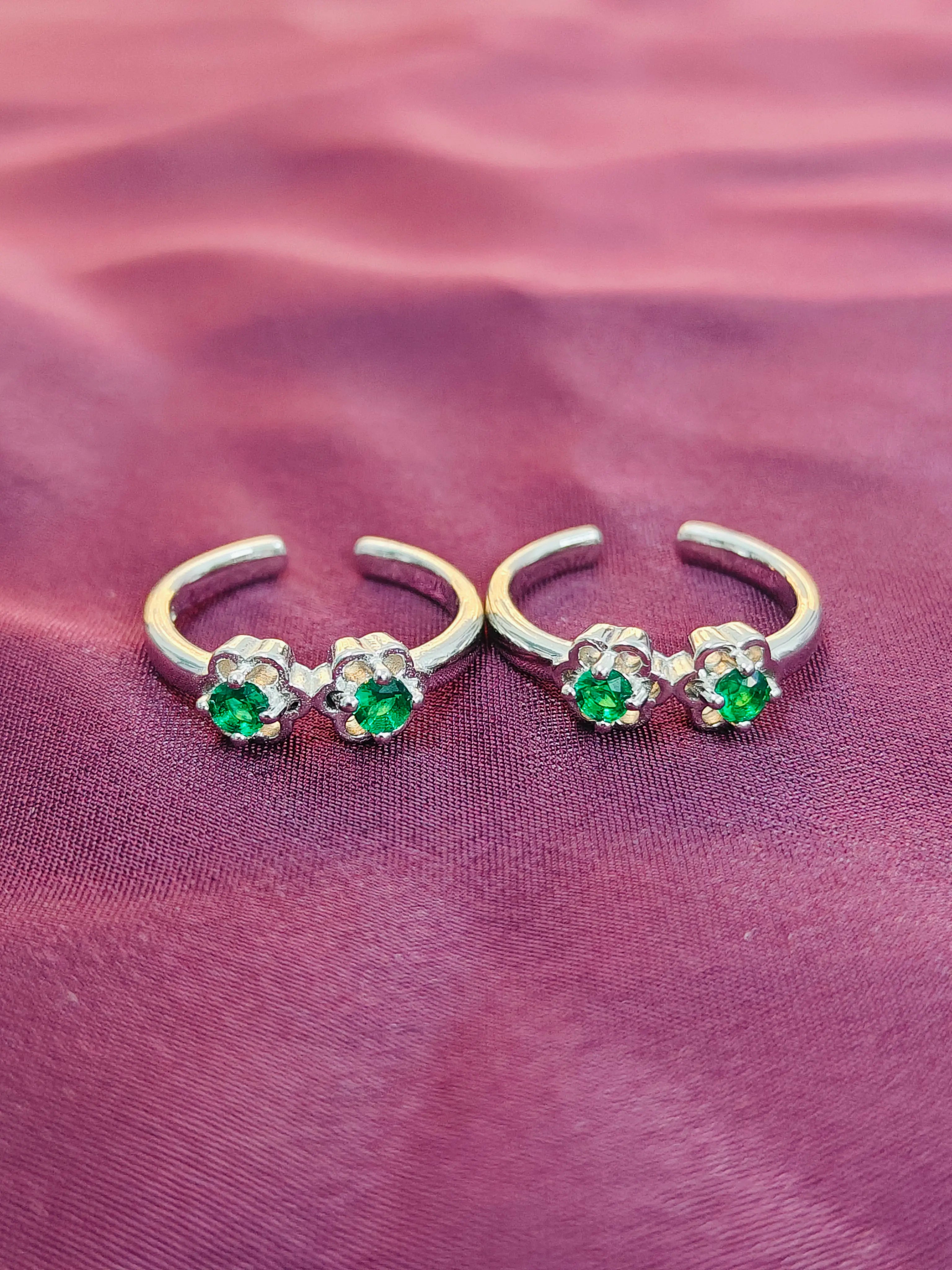 Pair of silver rings with green gemstones on a purple fabric background