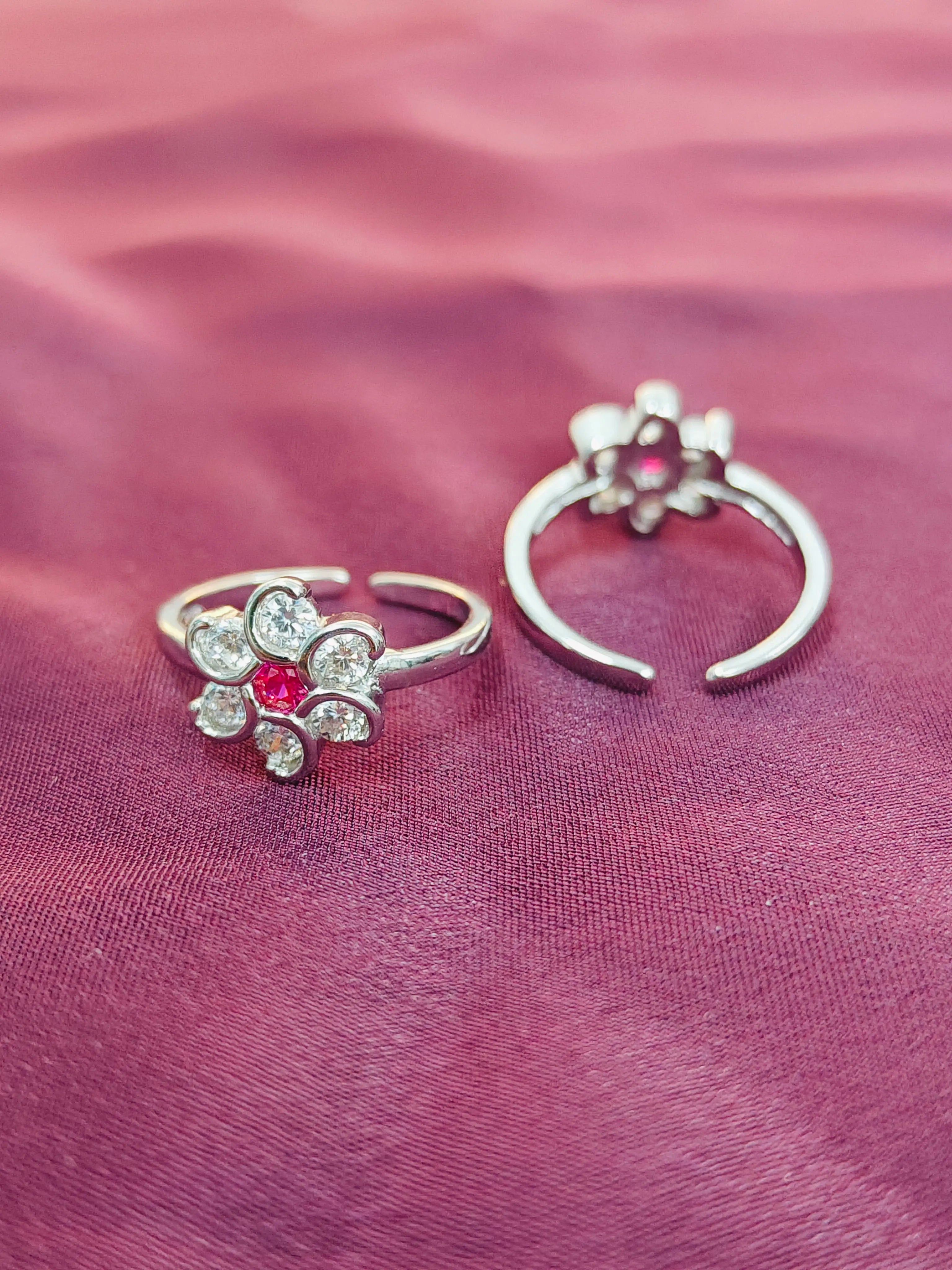 Two silver floral rings with red gemstones on a pink fabric background