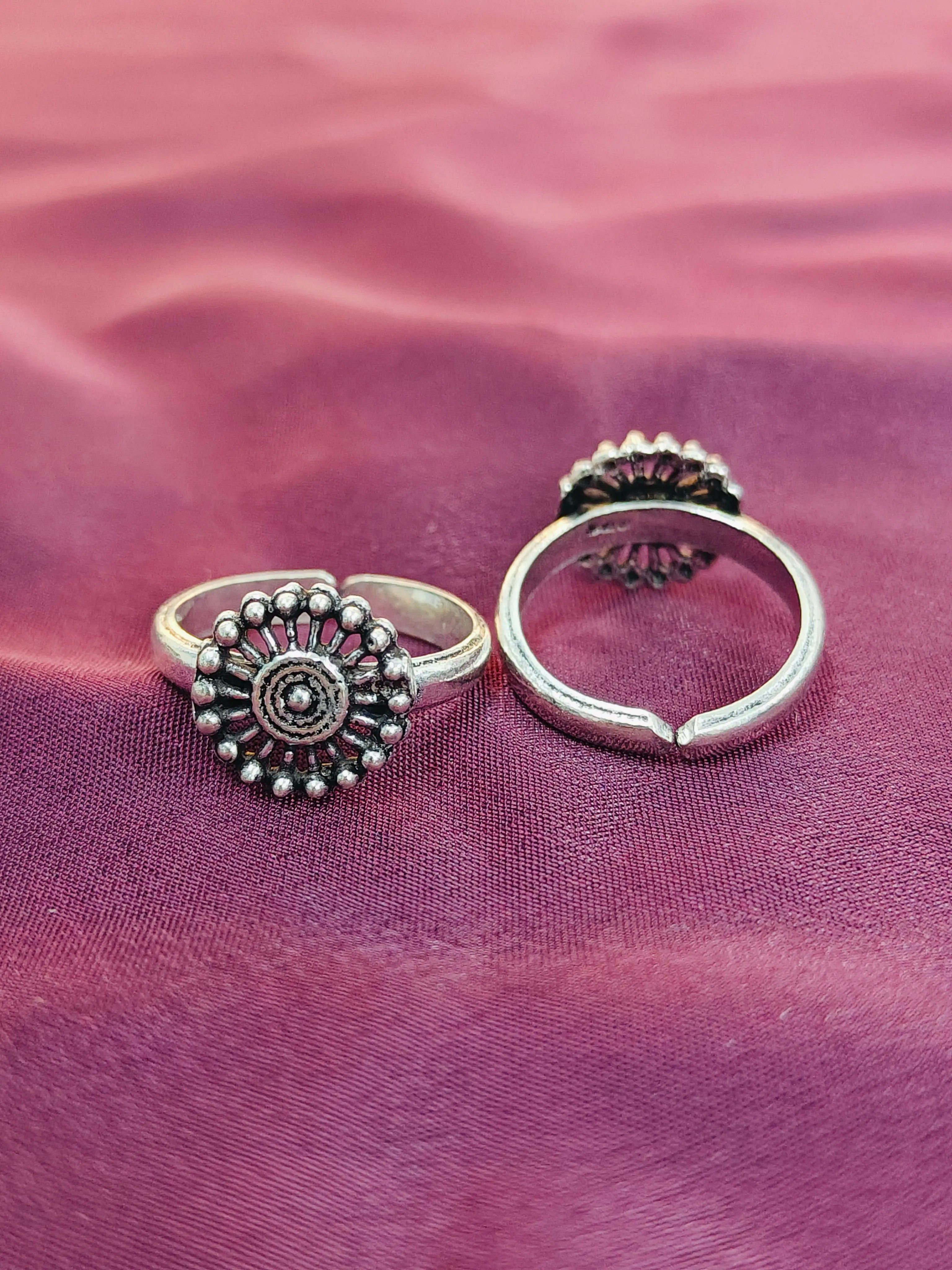 Two silver rings with intricate designs on a purple fabric background