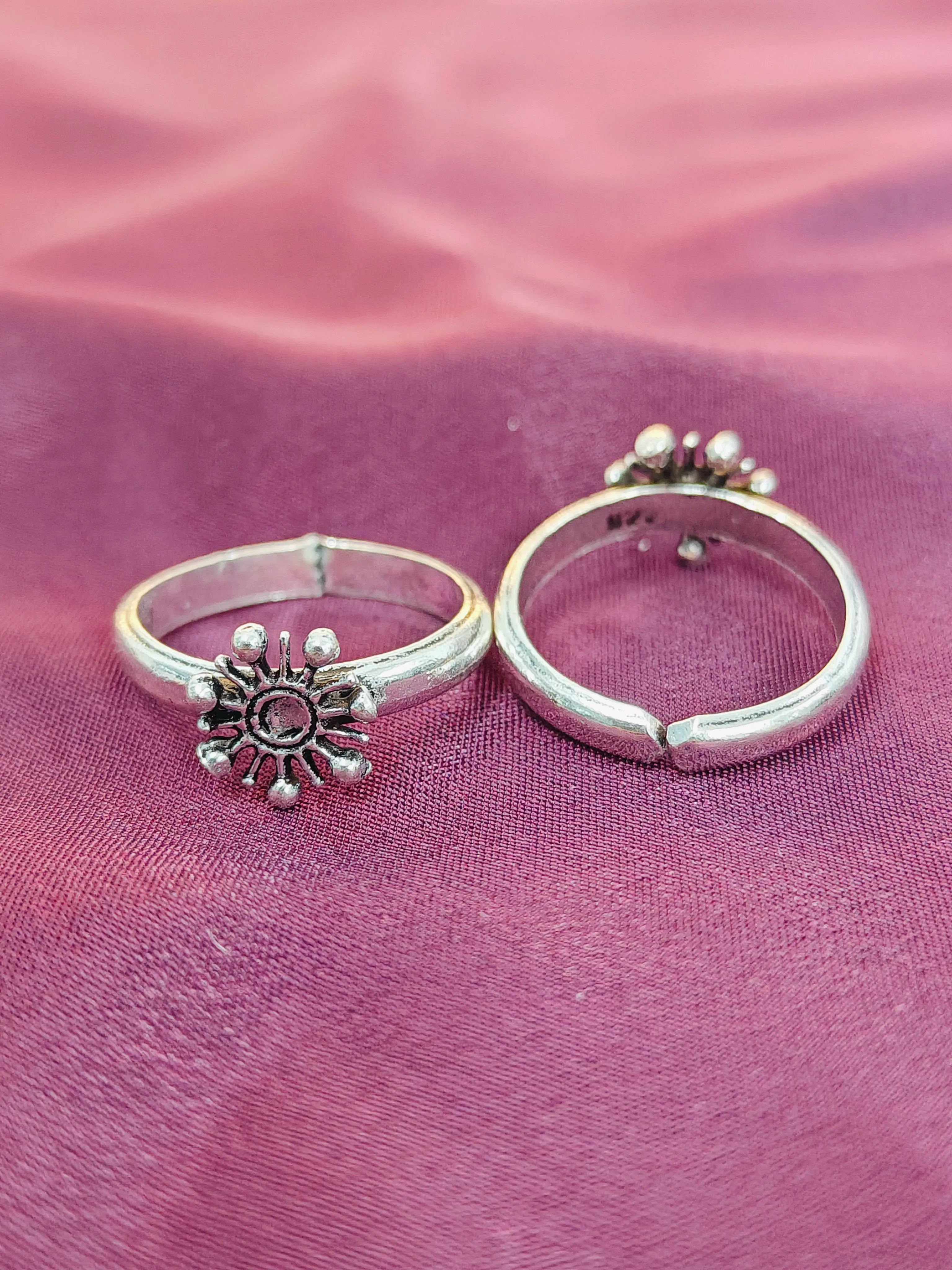 Two silver rings with decorative designs on a pink fabric background