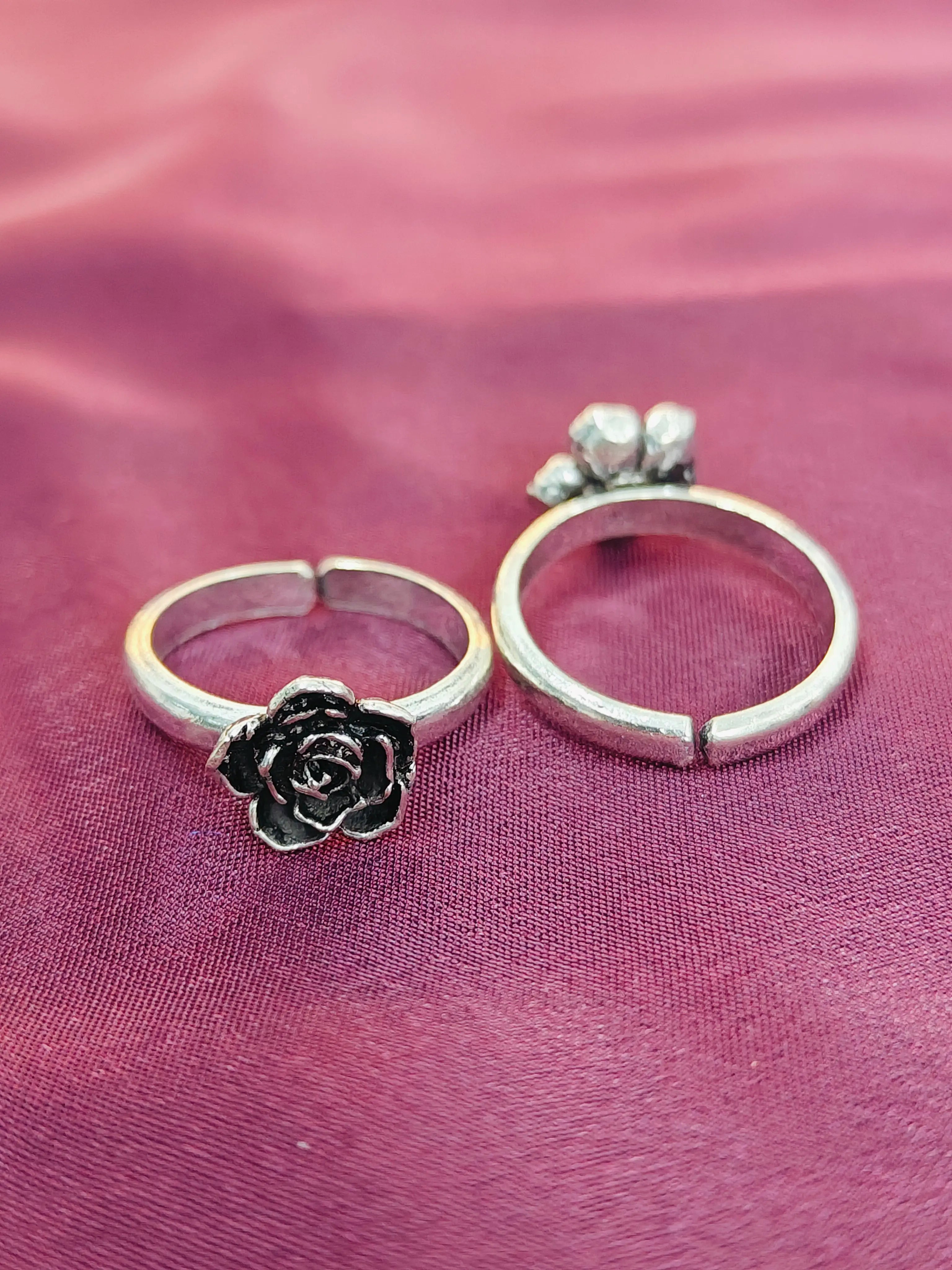 Two silver rings with floral designs on a pink fabric background