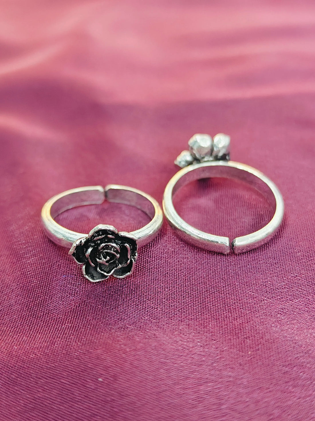 Two silver rings with floral designs on a pink fabric background