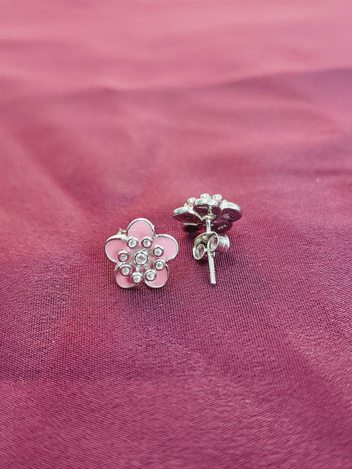 Pink flower-shaped earrings with clear stones on a pink fabric background
