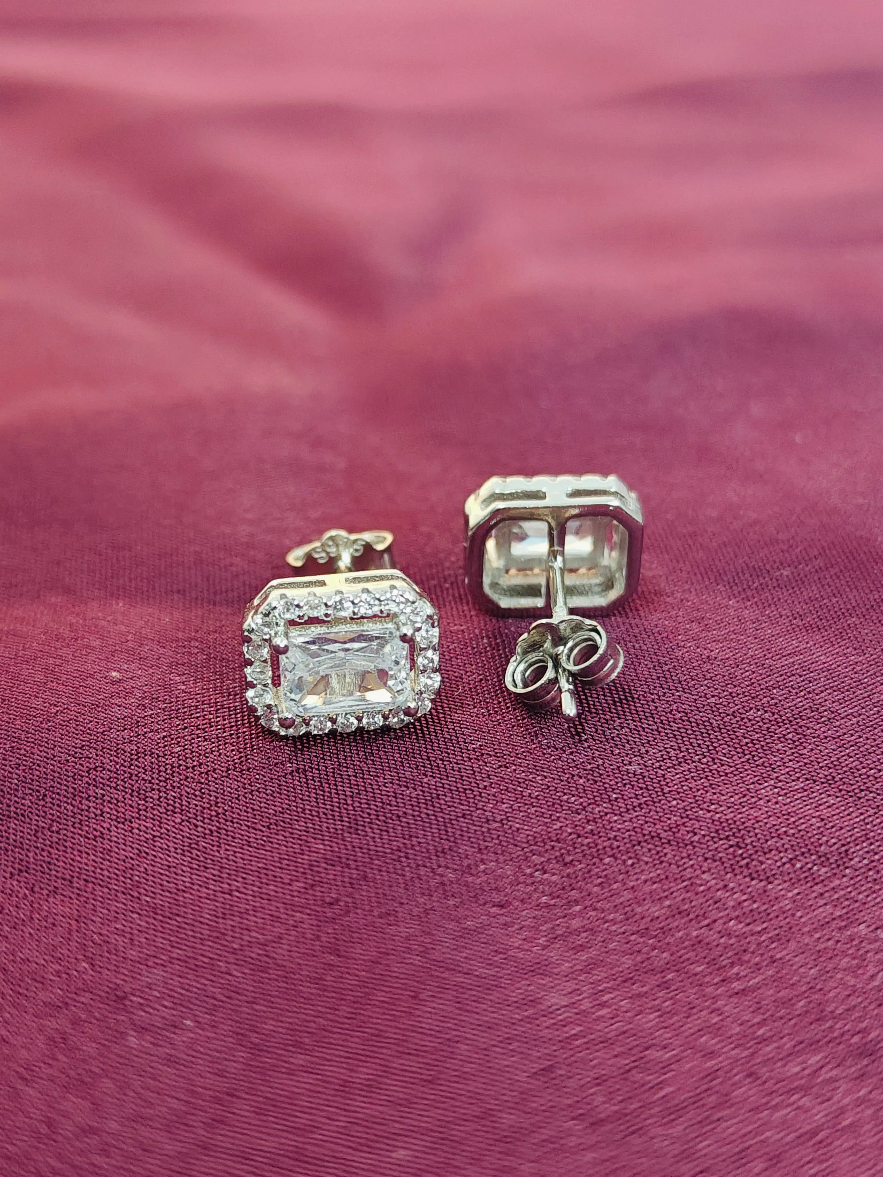 Silver earrings with gemstones on a maroon fabric background