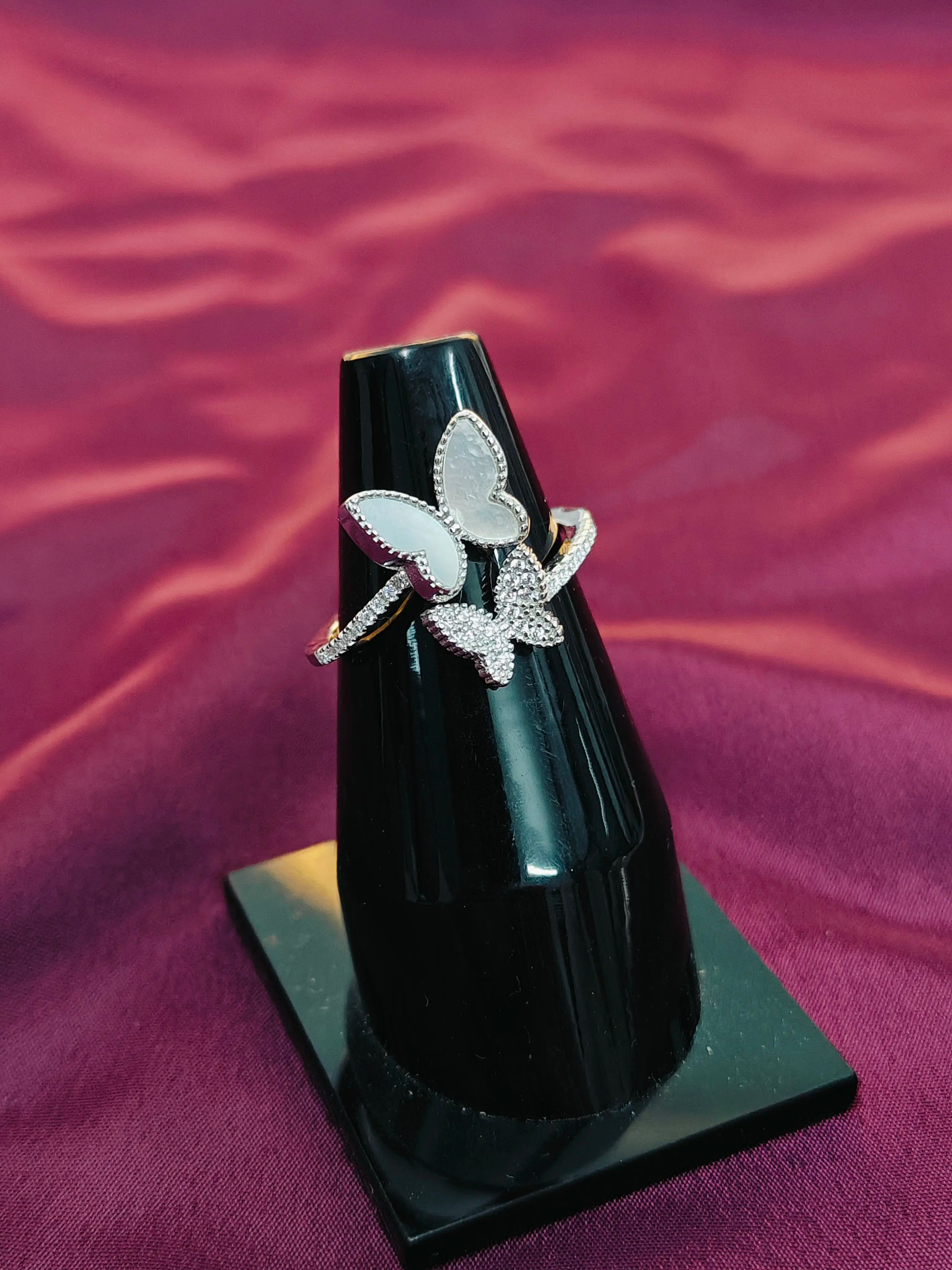 Butterfly ring on a black stand against a purple fabric background