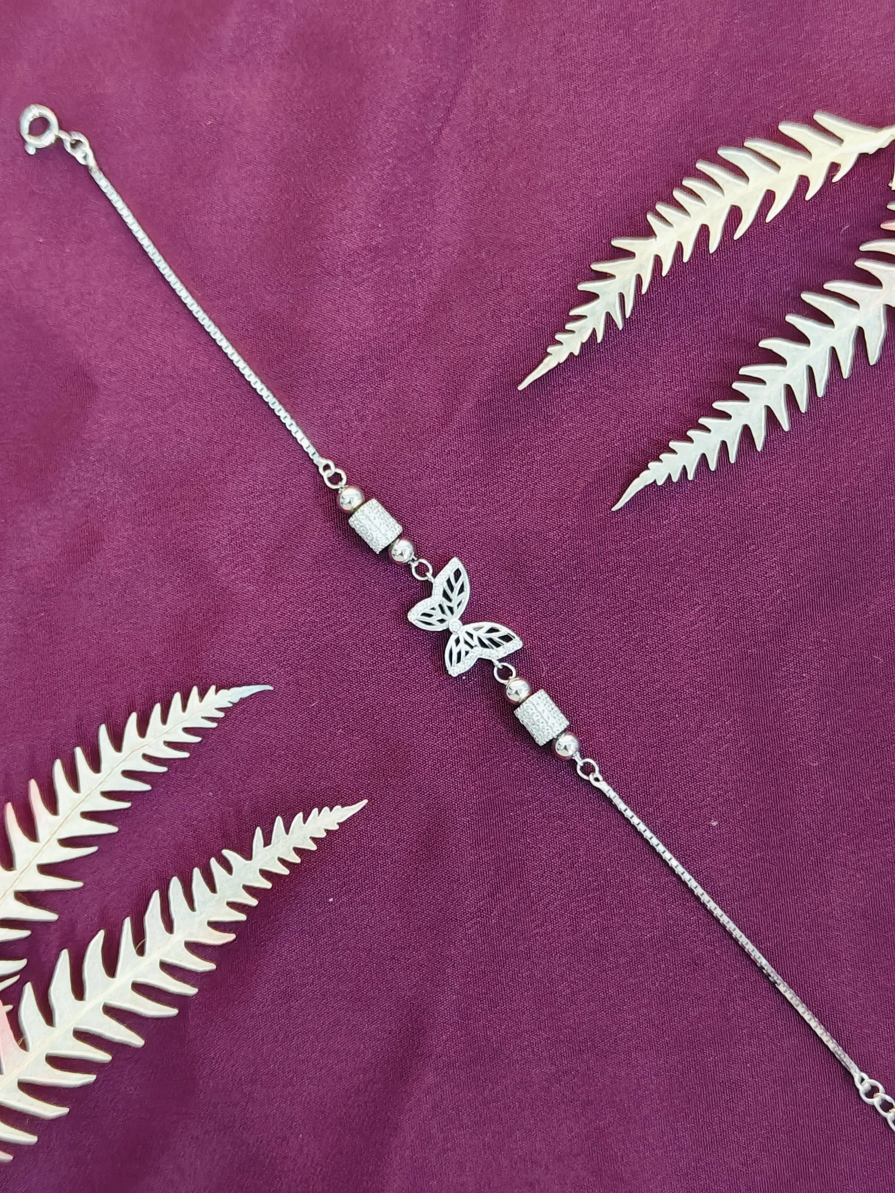 Silver butterfly bracelet on a purple fabric background with white leaf patterns