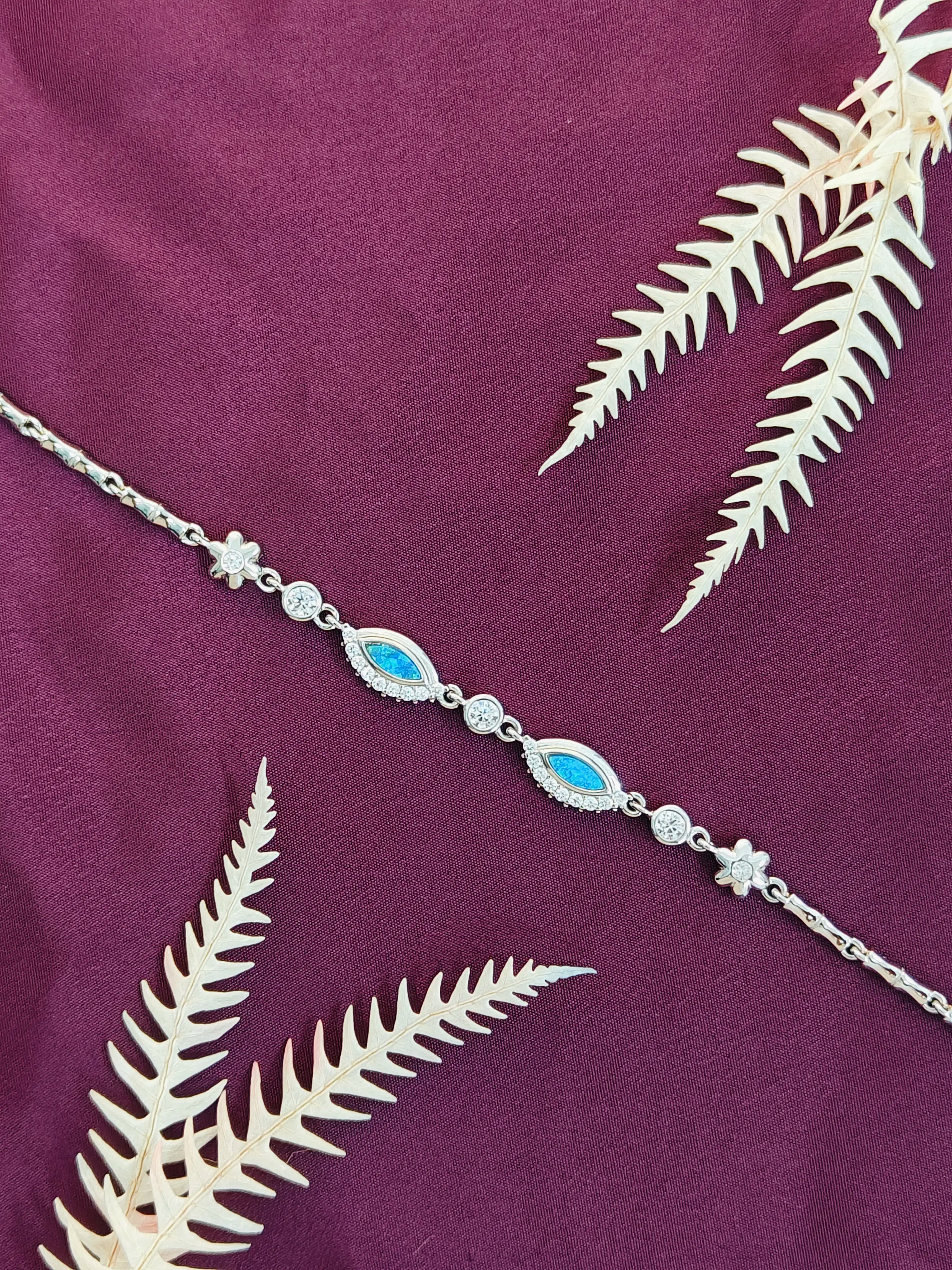 Silver bracelet with blue stones on a purple fabric background with white leaves